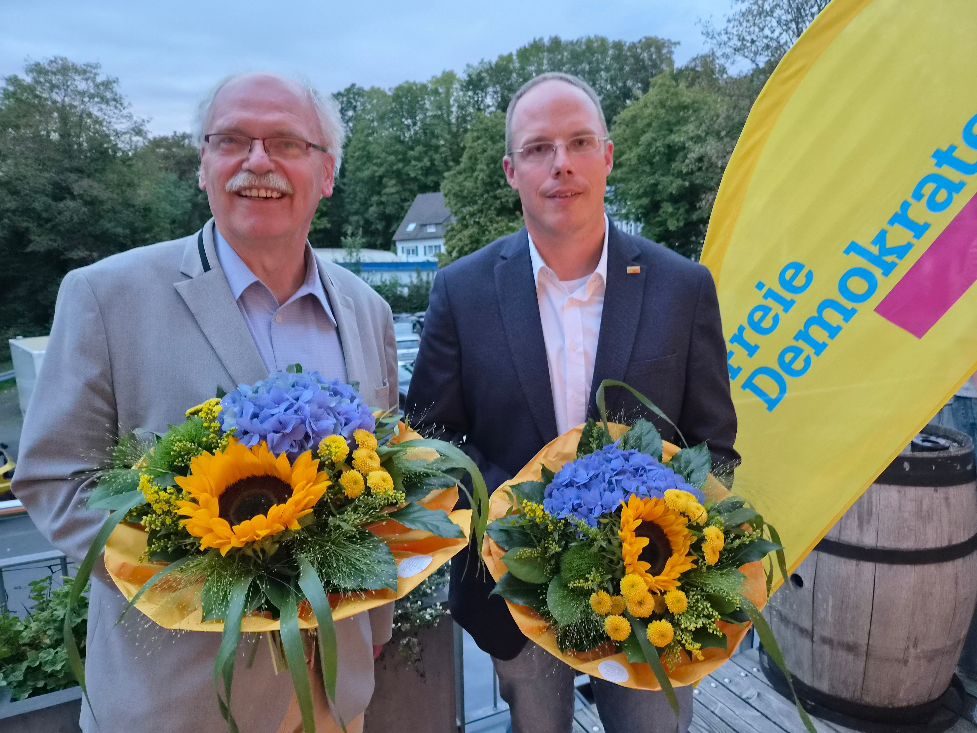 Zwei Herren mit Blumensträußen.