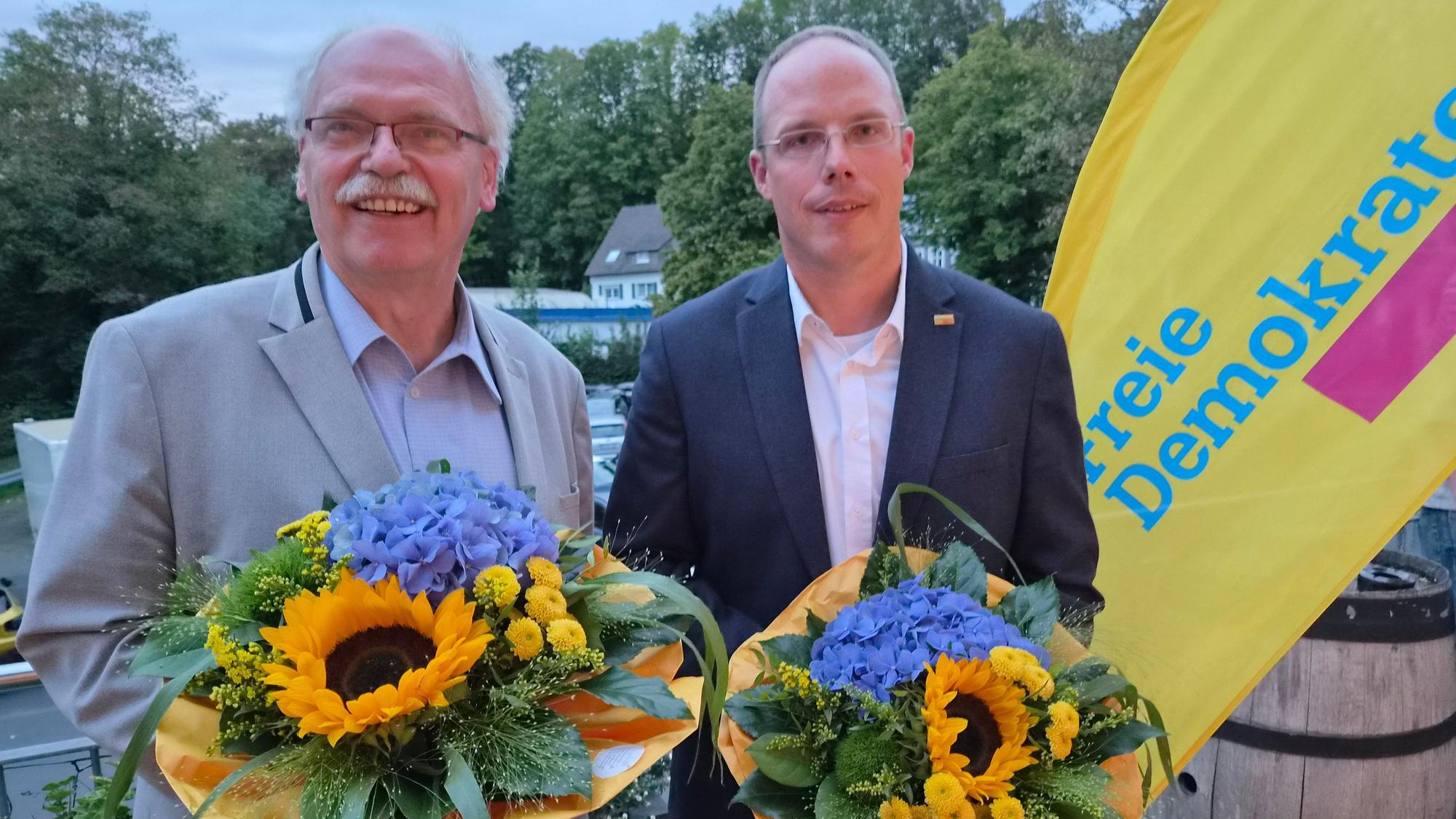 Zwei Herren mit Blumensträußen.