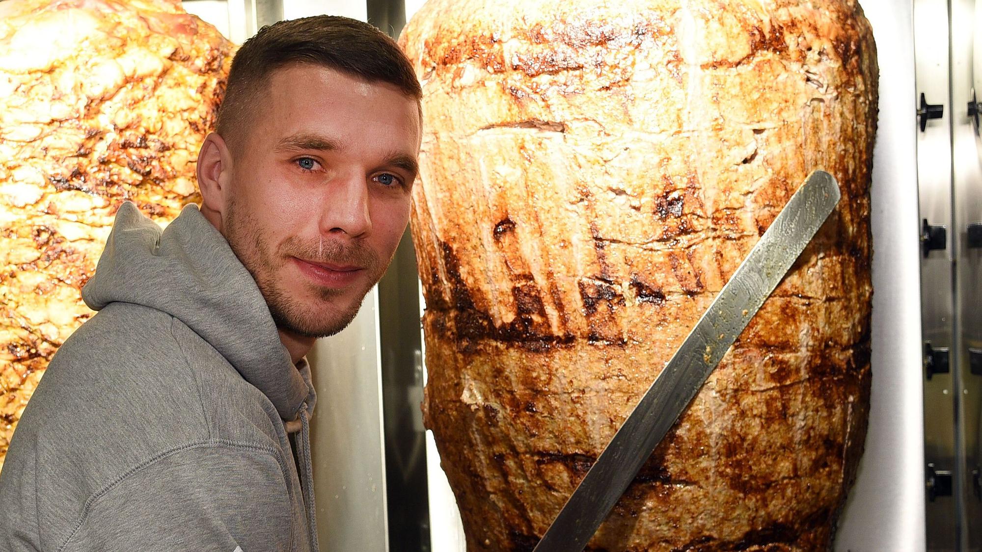 Lukas Podolski steht bei der Eröffnung eines Dönerladens an einem Dönerspieß.