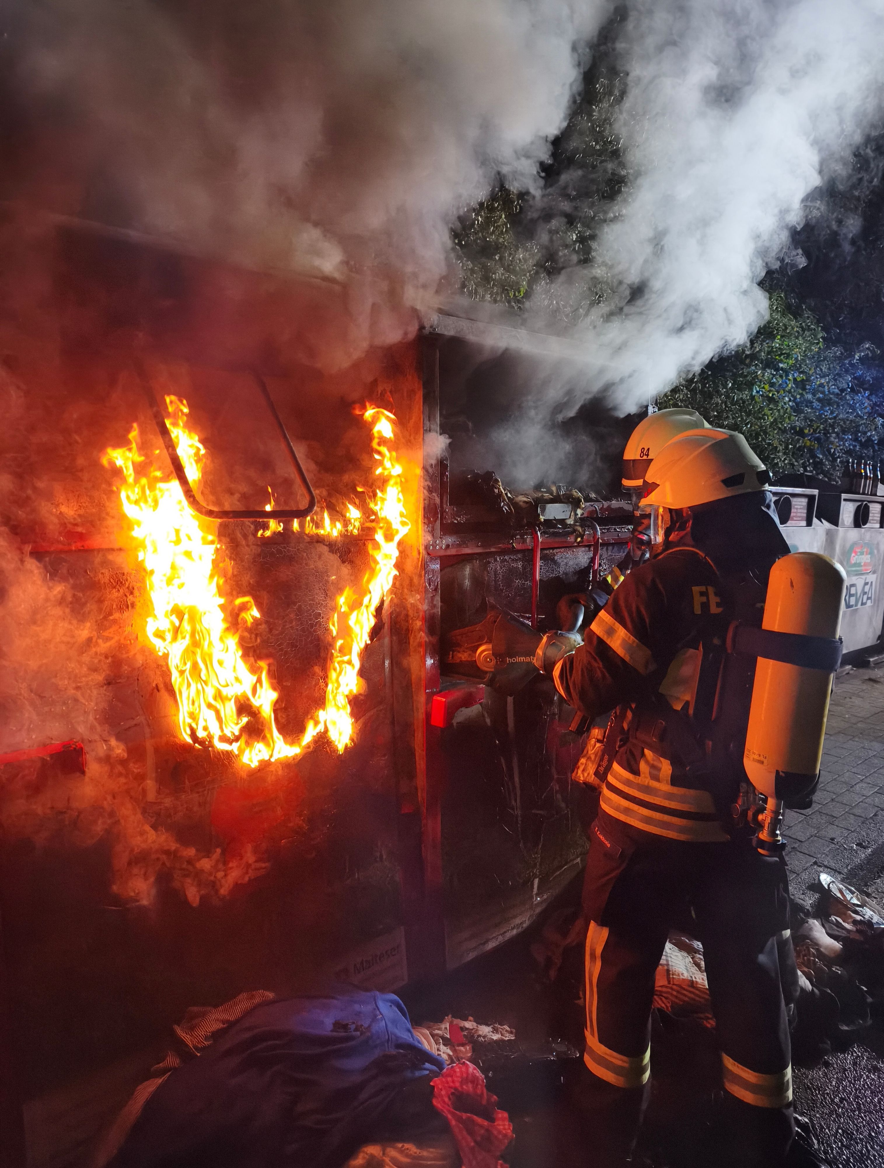 Ein Feuerwehrmann löscht einen brennenden Altkleidercontainer.