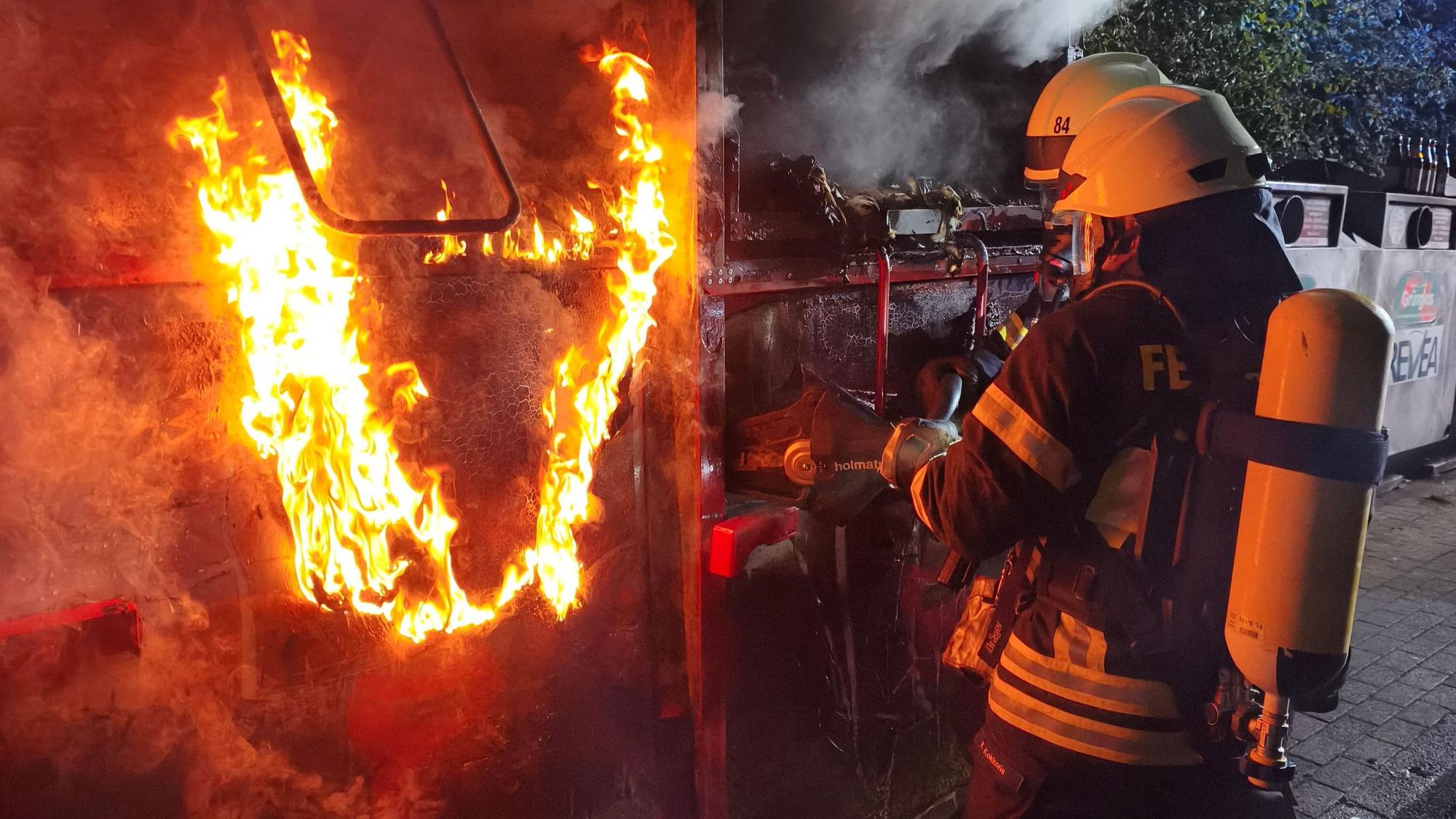 Ein Feuerwehrmann löscht einen brennenden Altkleidercontainer.