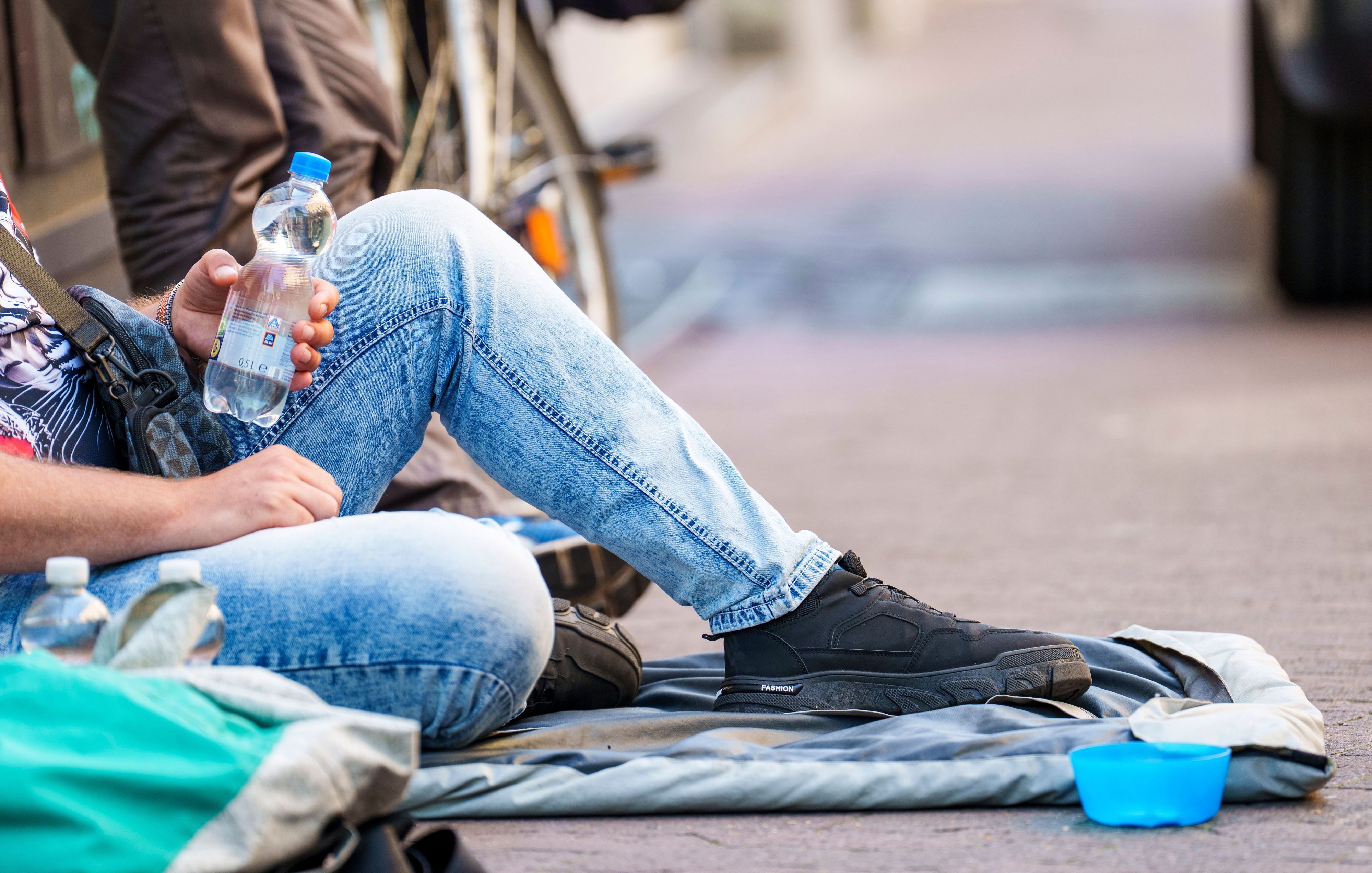 Ein Obdachloser sitzt und hält eine Wasserflasche.