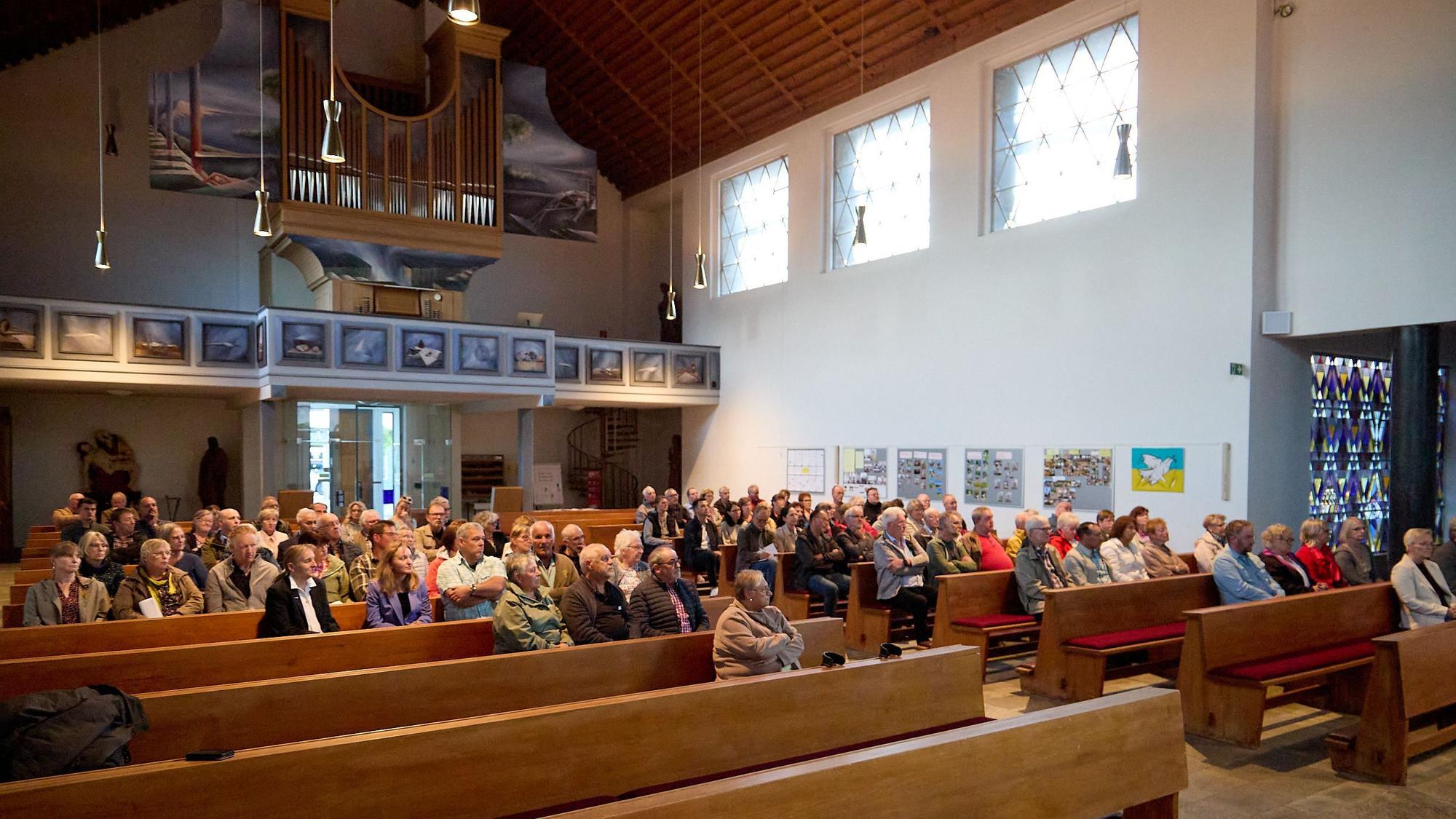 Blick in den Kirchenraum mit den gefüllten Sitzreihen. Darüber die Orgelempore.