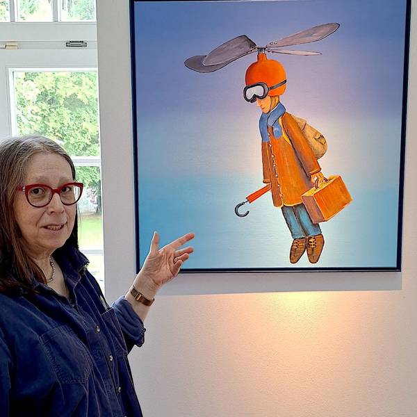Eine Frau zeigt auf ein Bild mit einer Figur, die einen Helm mit Propeller trägt.