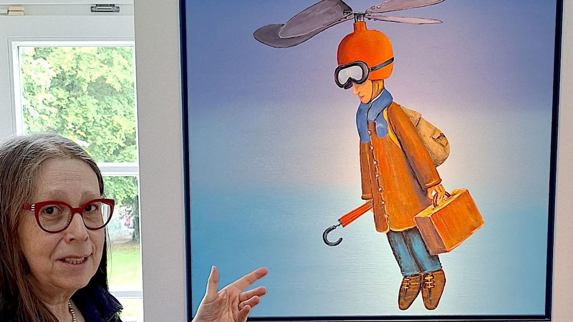 Eine Frau zeigt auf ein Bild mit einer Figur, die einen Helm mit Propeller trägt.