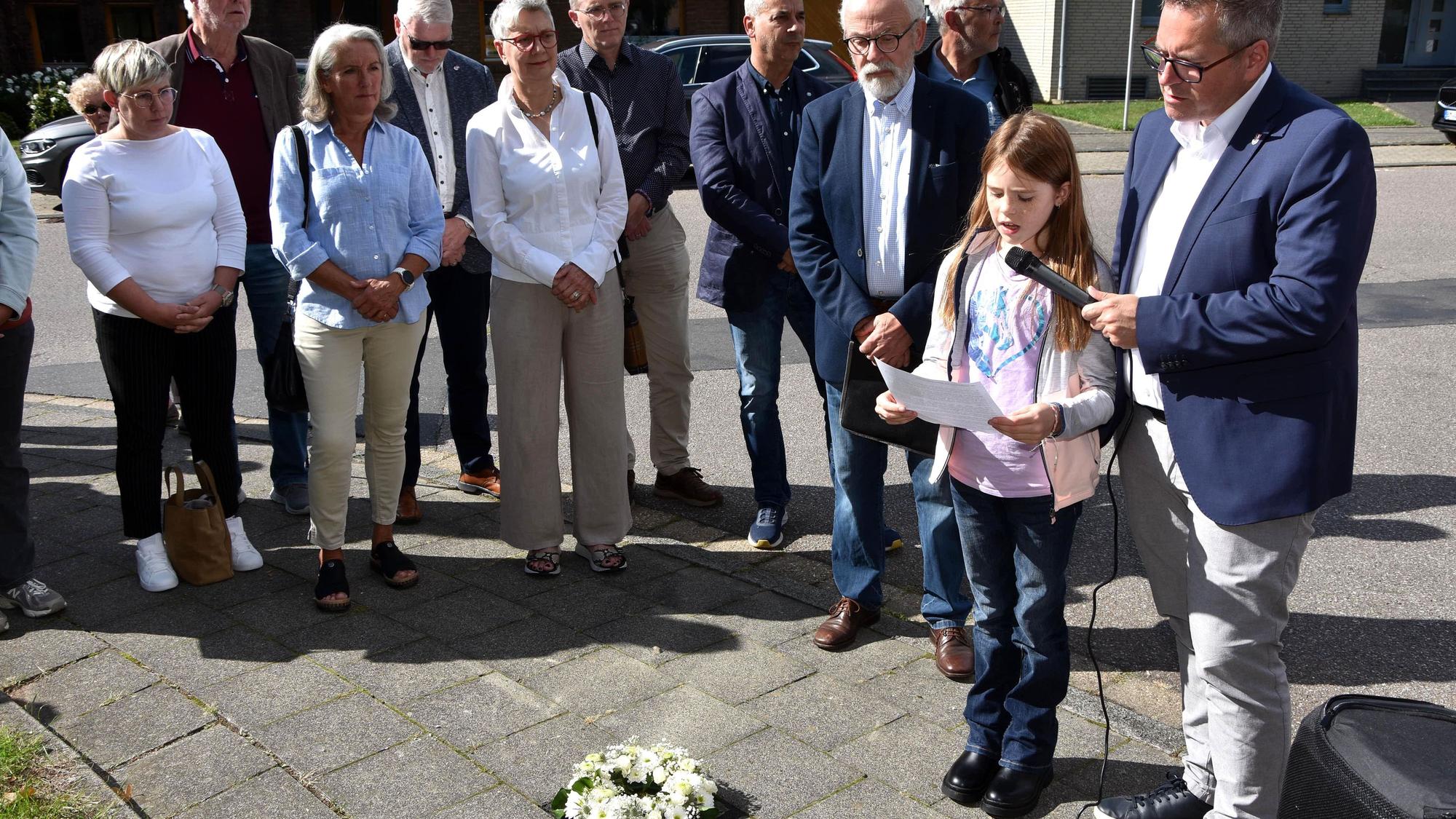 Zu sehen ist eine von Menschen umgebene Schülerin, die bei einer Stolperstein-Verlegung einen Text vorträgt.