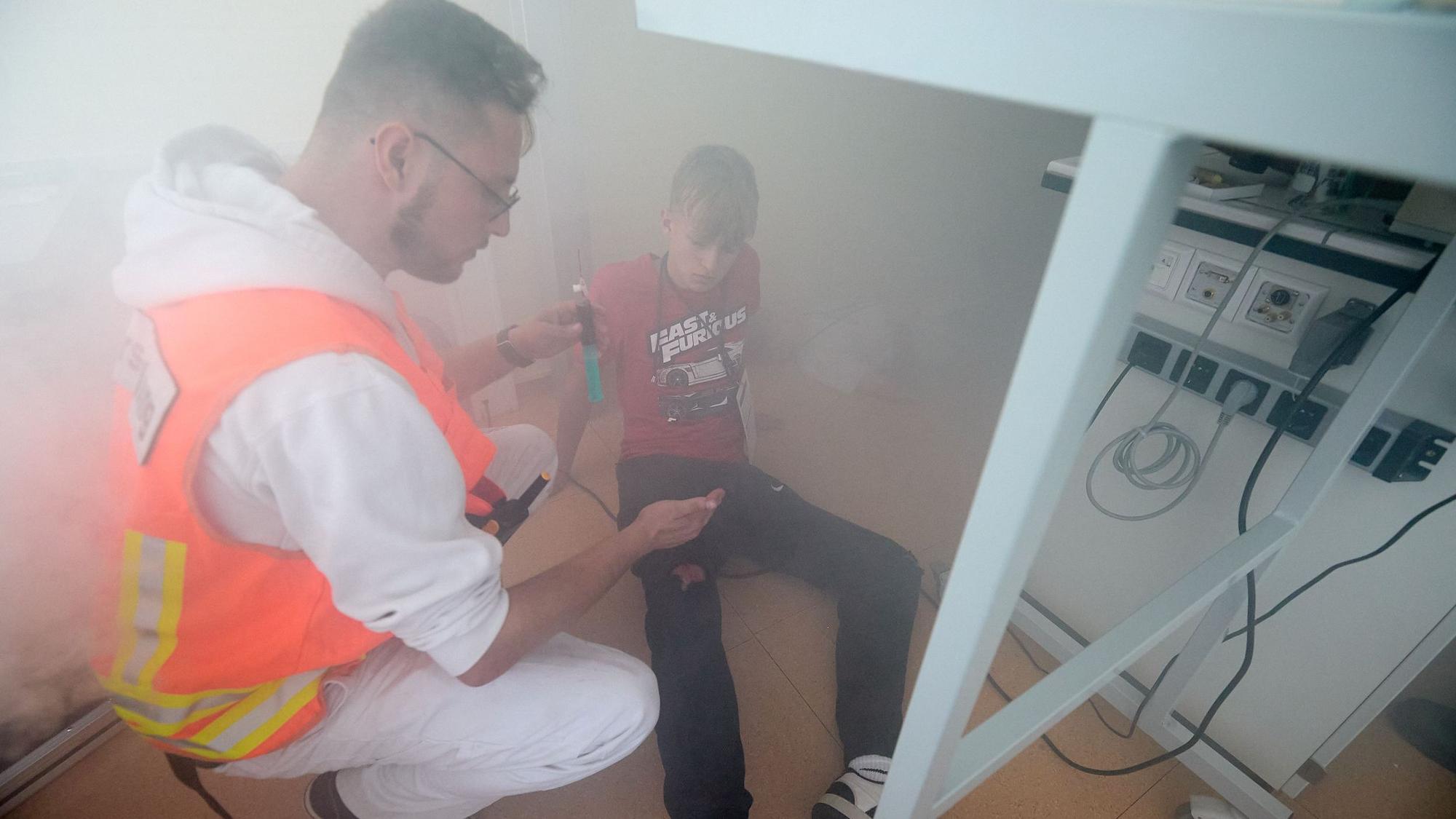 Ein Mann in orangefarbener Warnweste hockt in einem vernebelten Raum neben einem Jugendlichen.