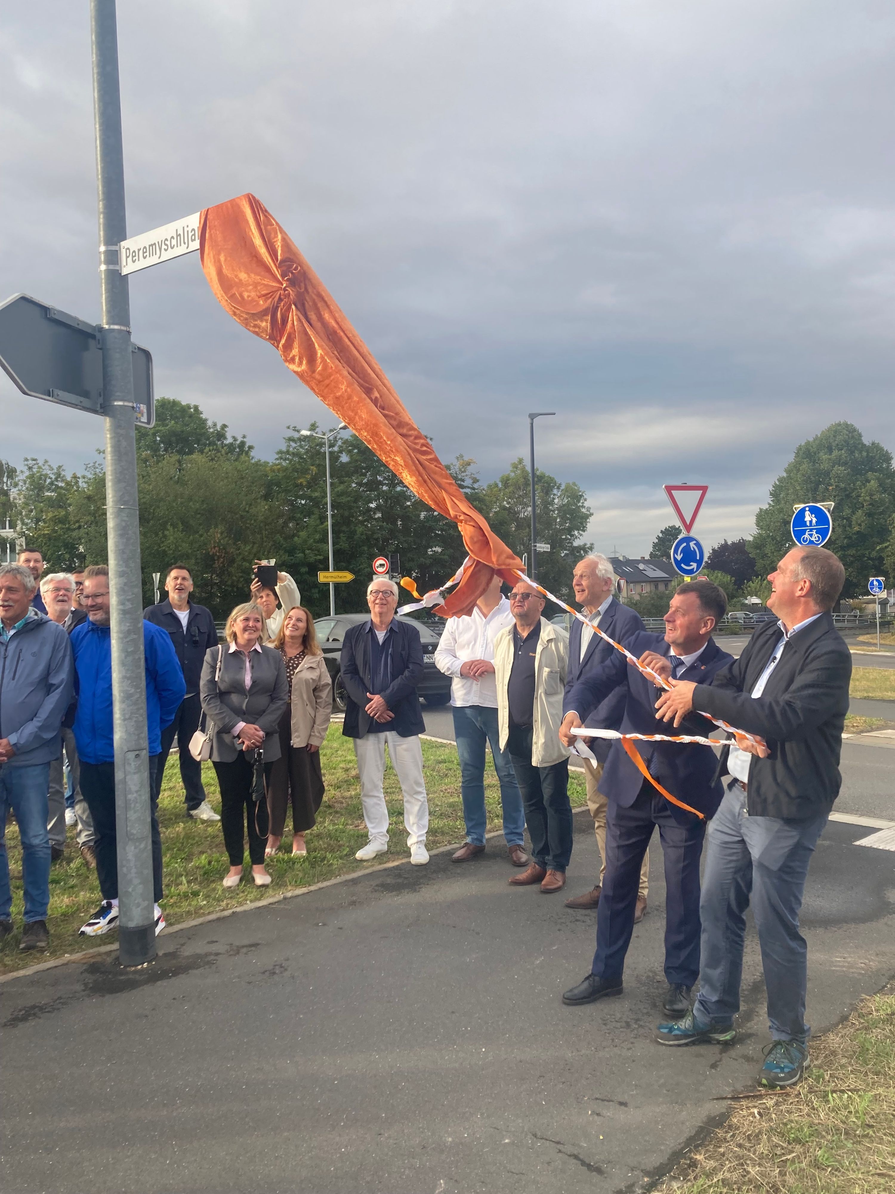 Das Foto zeigt eine Gruppe von Menschen bei der Enthüllung eines Straßenschilds.