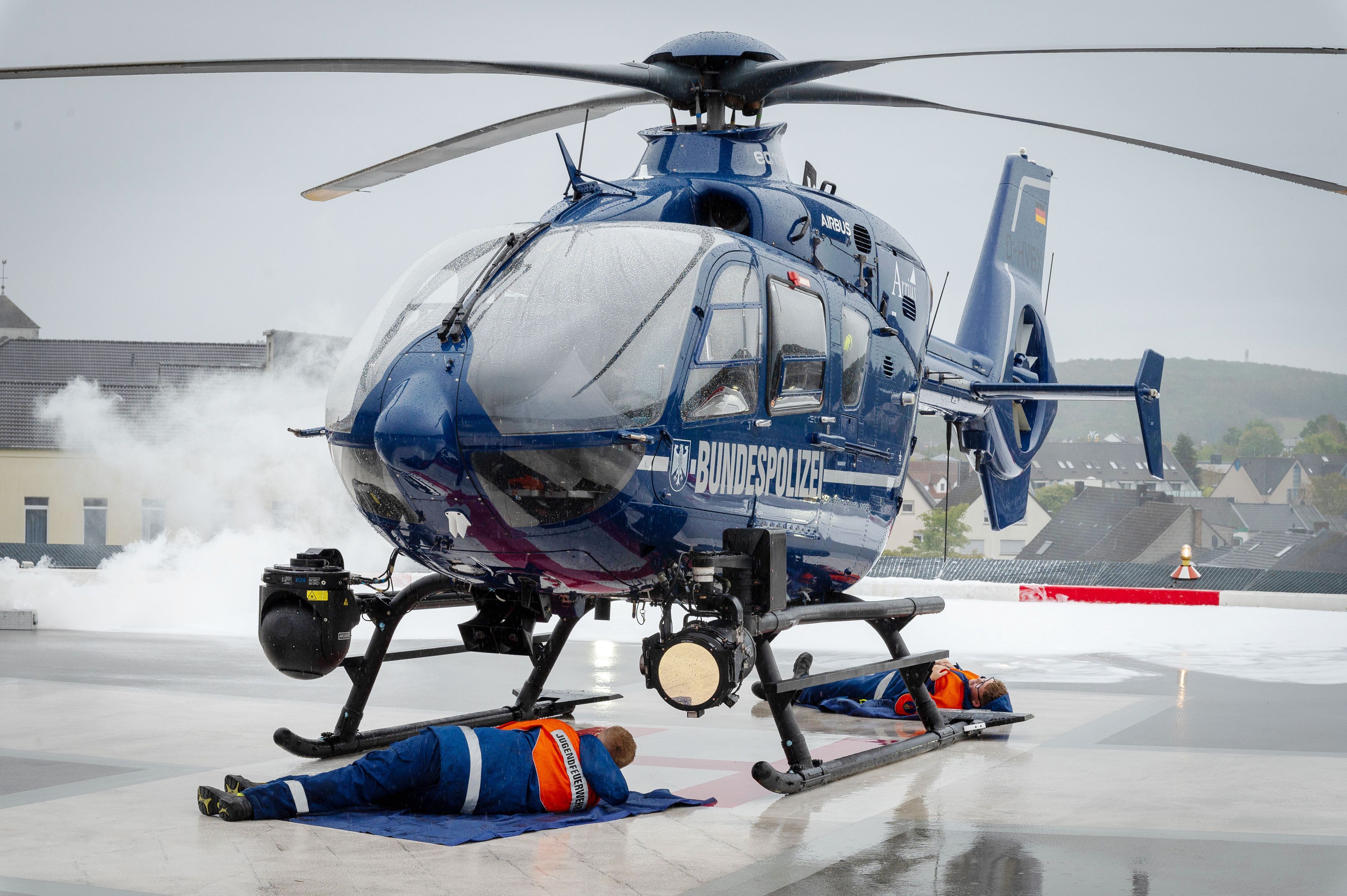 Im Rahmen einer Übung steht ein Helikopter der Bundespolizei auf dem Hubschrauberlandeplatz des Kreiskrankenhaus Mechernich. Zwei Jugendfeuerwehrleute liegen darunter und mimen Verletzte, mit Pyrotechnik wird Rauch erzeugt.