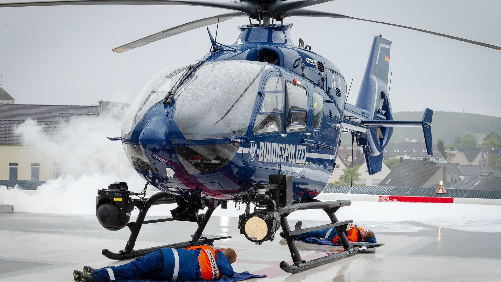Im Rahmen einer Übung steht ein Helikopter der Bundespolizei auf dem Hubschrauberlandeplatz des Kreiskrankenhaus Mechernich. Zwei Jugendfeuerwehrleute liegen darunter und mimen Verletzte, mit Pyrotechnik wird Rauch erzeugt.