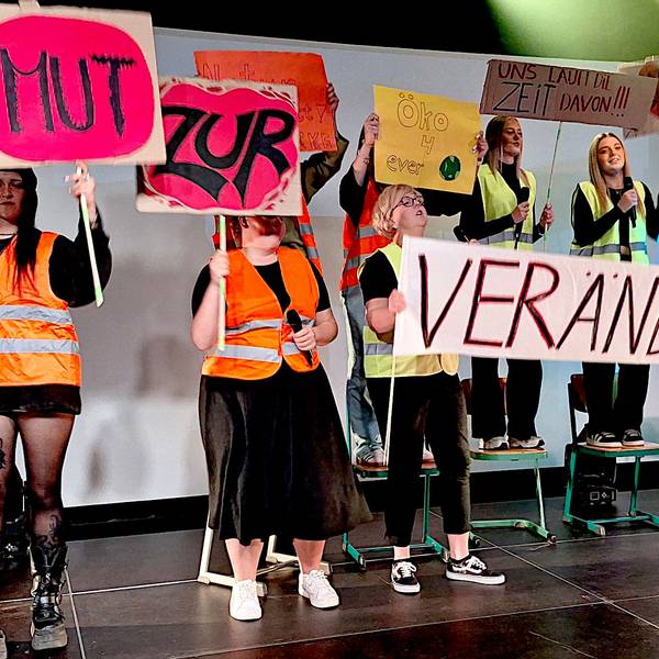 Mehre junge Frauen stehen in Warnwesten auf einer Bühne und halten Schilder in der Hand.