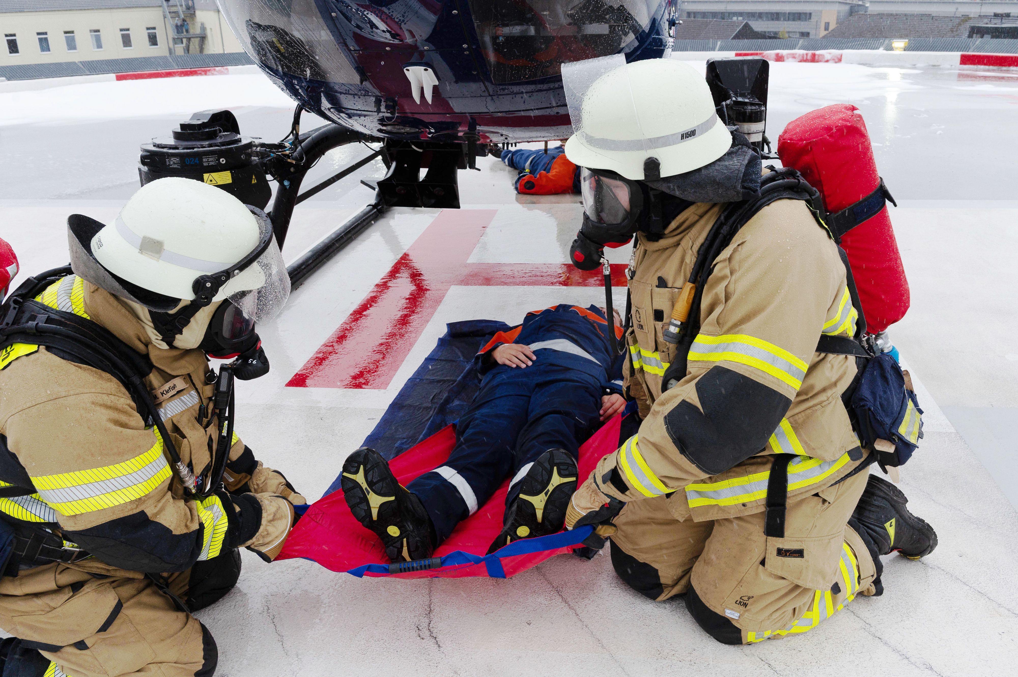 Zwei Feuerwehrleute ziehen einen Jugendlichen, der im Rahmen einer Übung in Mechernich einen Verletzten darstellt, mit einem Rettungstuch unter einem Helikopter hervor.