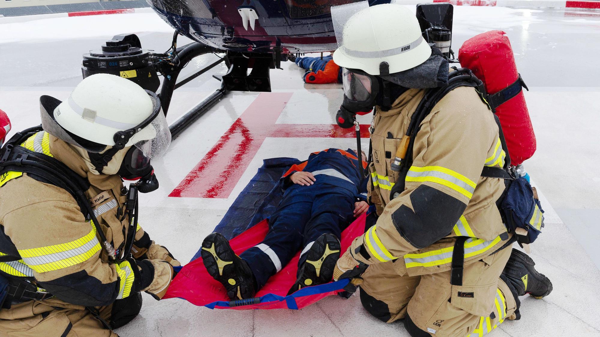Zwei Feuerwehrleute ziehen einen Jugendlichen, der im Rahmen einer Übung in Mechernich einen Verletzten darstellt, mit einem Rettungstuch unter einem Helikopter hervor.