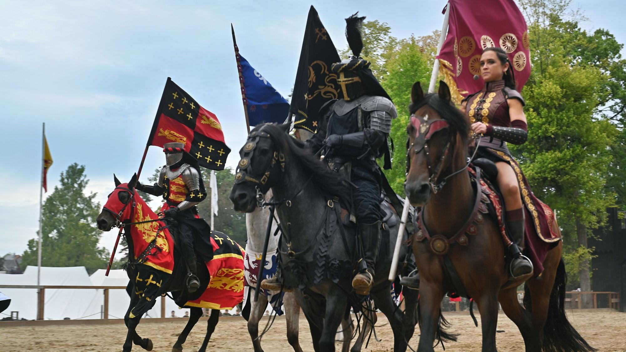 In prunkvollen Rüstungen reiten die Turnierteilnehmer über den Sand.