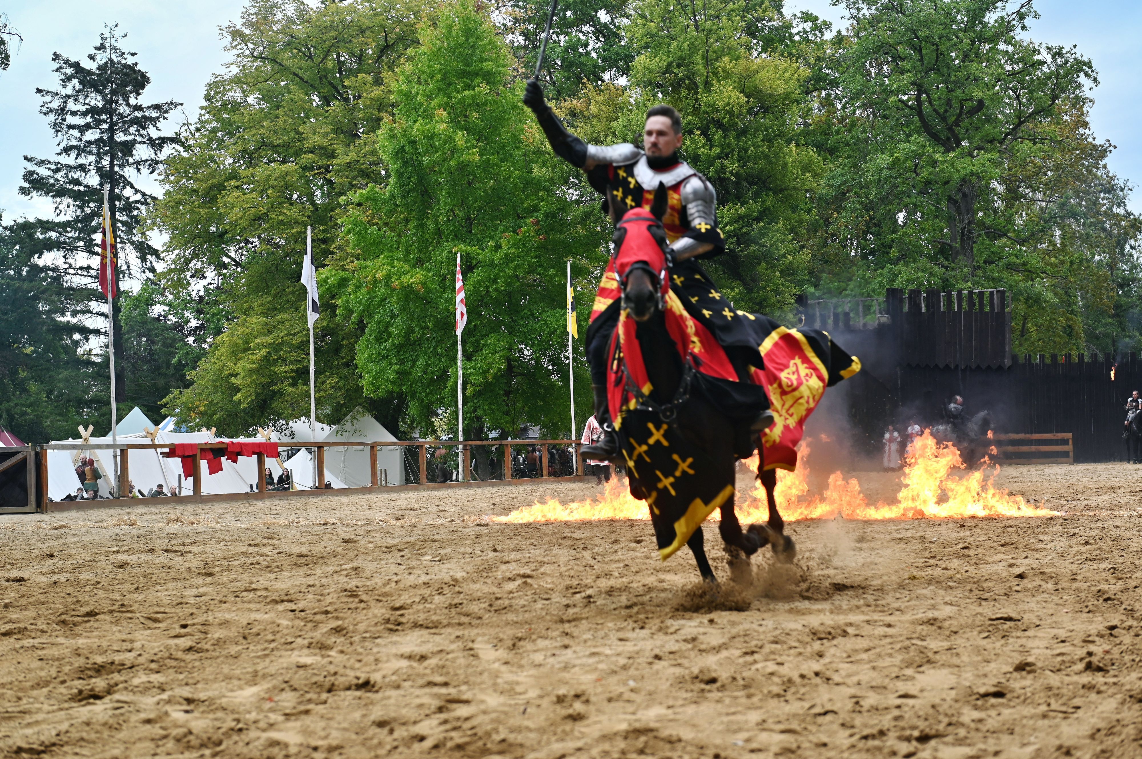 Ein Mann in Ritterrüstung reitet mit einem Pferd durch Feuer.