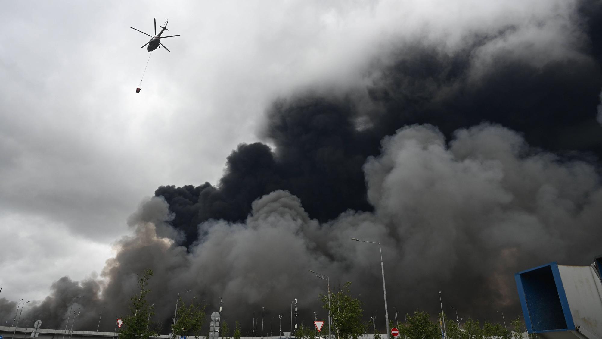 Ein Löschhubschrauber transportiert Wasser, während schwarzer Rauch aus dem Bereich der Moskauer Ölraffinerie von Gazprom Neft am südöstlichen Stadtrand von Moskau aufsteigt. Die Aufnahme entstand am 18. Juni 2026 nach einem von Moskaus Bürgermeister als großangelegten ukrainischen Drohnenangriff bezeichneten Angriff.