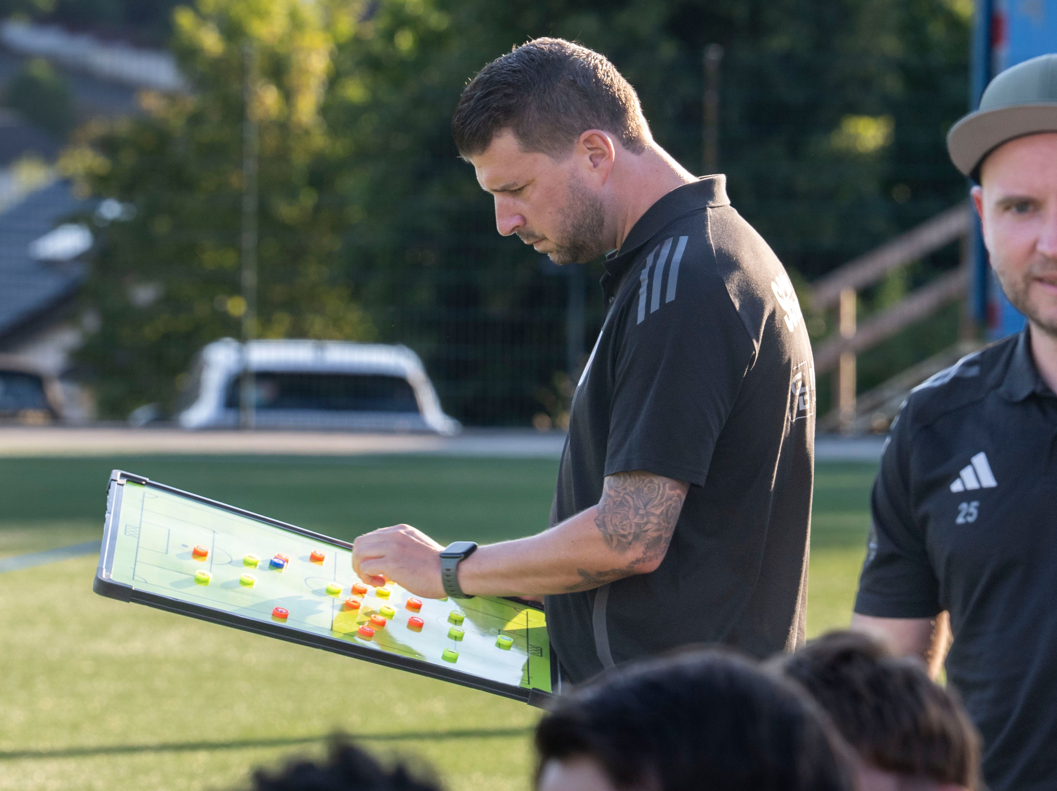 Das Bild zeigt den Trainer der SG Dahlem-Schmidtheim am Spielfeldrand. Er hat eine Taktiktafel in den Händen.