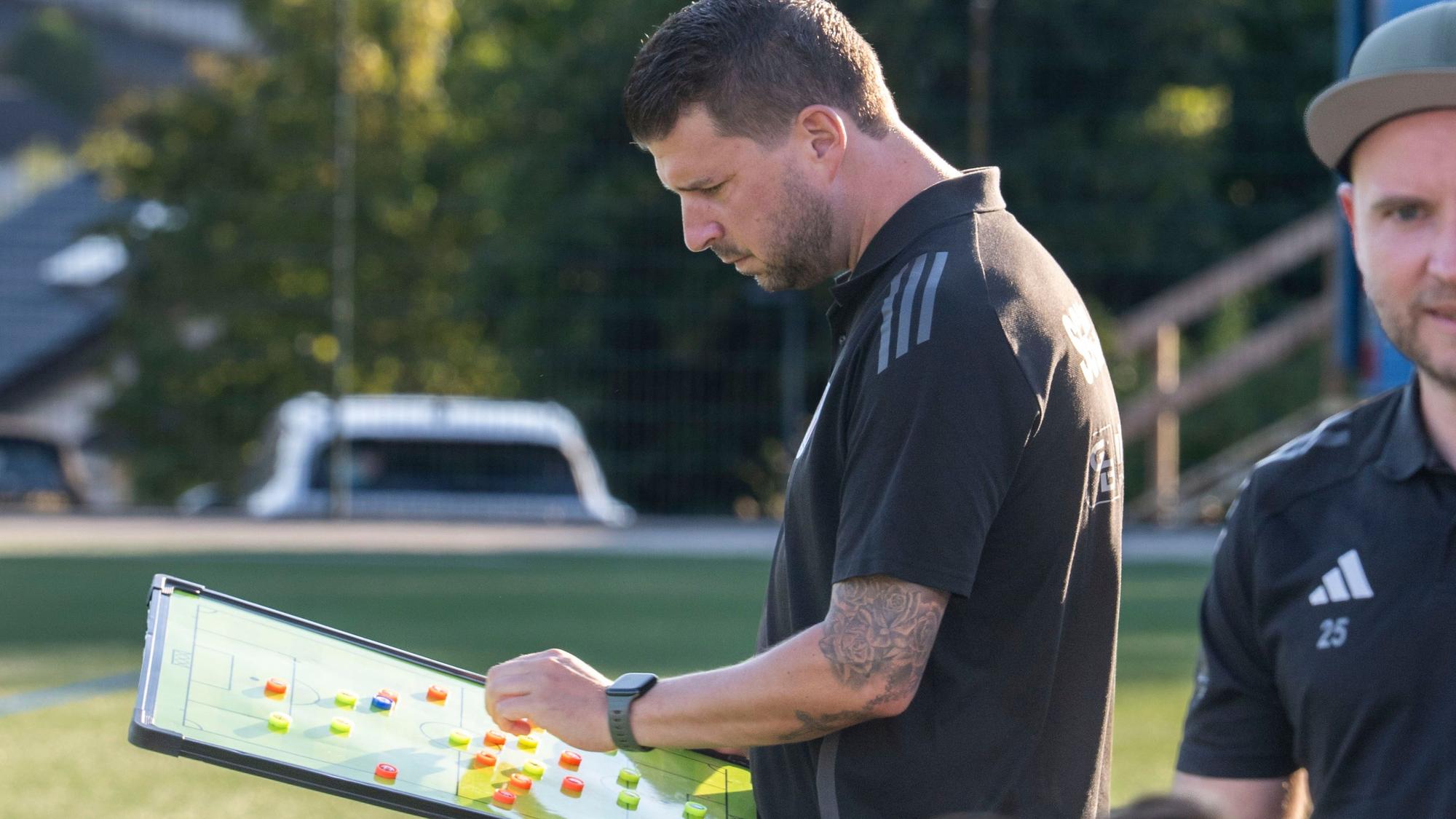 Das Bild zeigt den Trainer der SG Dahlem-Schmidtheim am Spielfeldrand. Er hat eine Taktiktafel in den Händen.