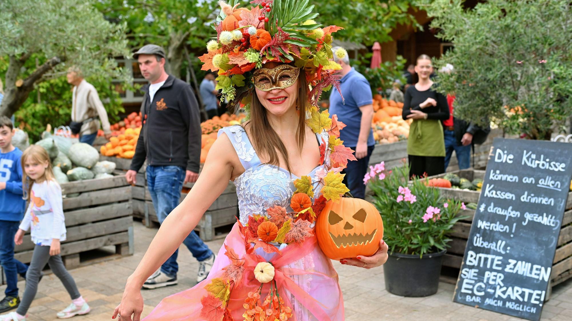 Kürbiskönigin Nataliia trägt einen Halloween-Kürbis in der Hand und ein Kleid sowie Kopfschmuck mit Herbstlaub und kleinen Kürbissen.