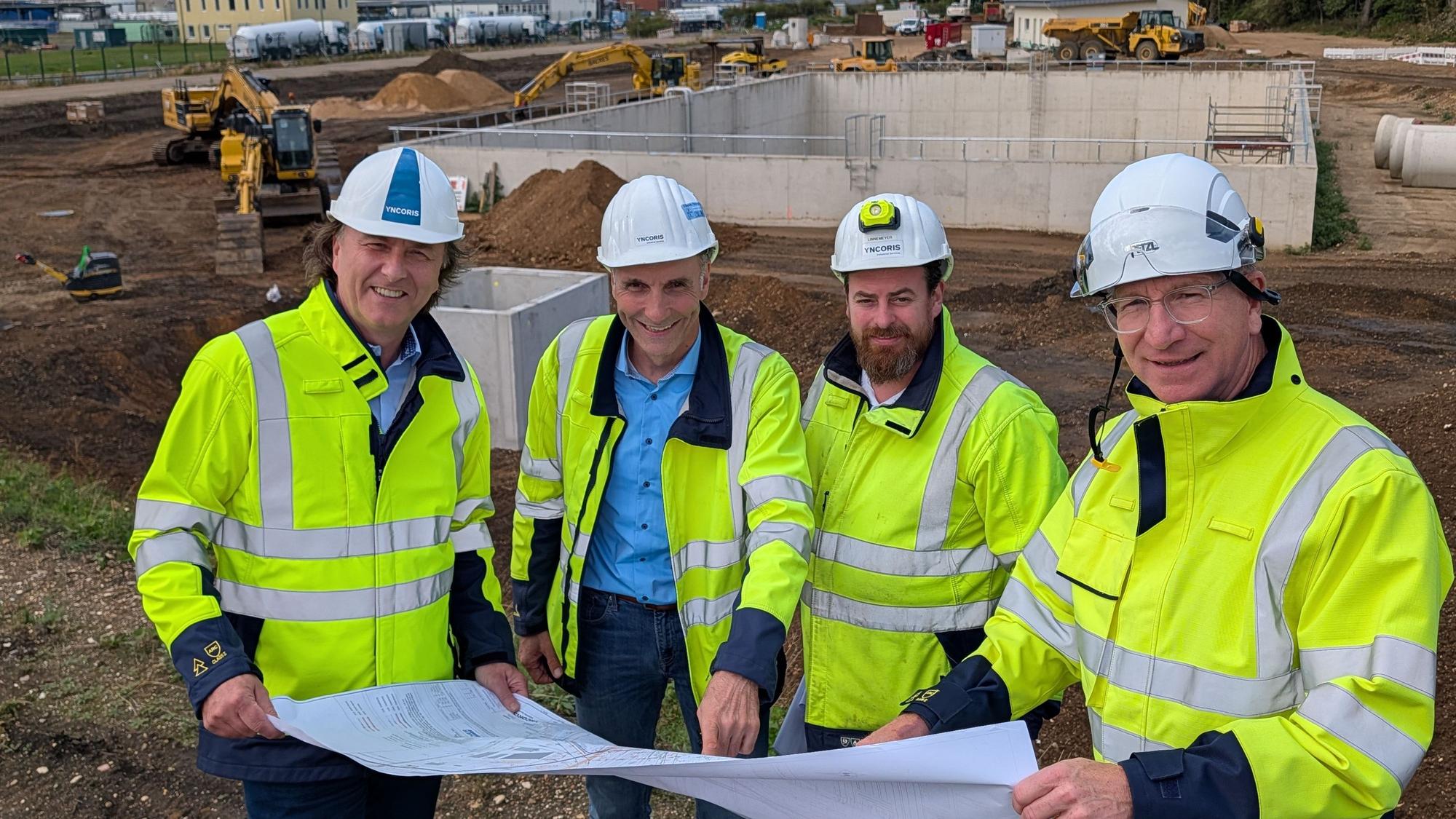 Das Foto zeigt vier Männer mit Helmen und Sicherheitswesten auf der Baustelle.