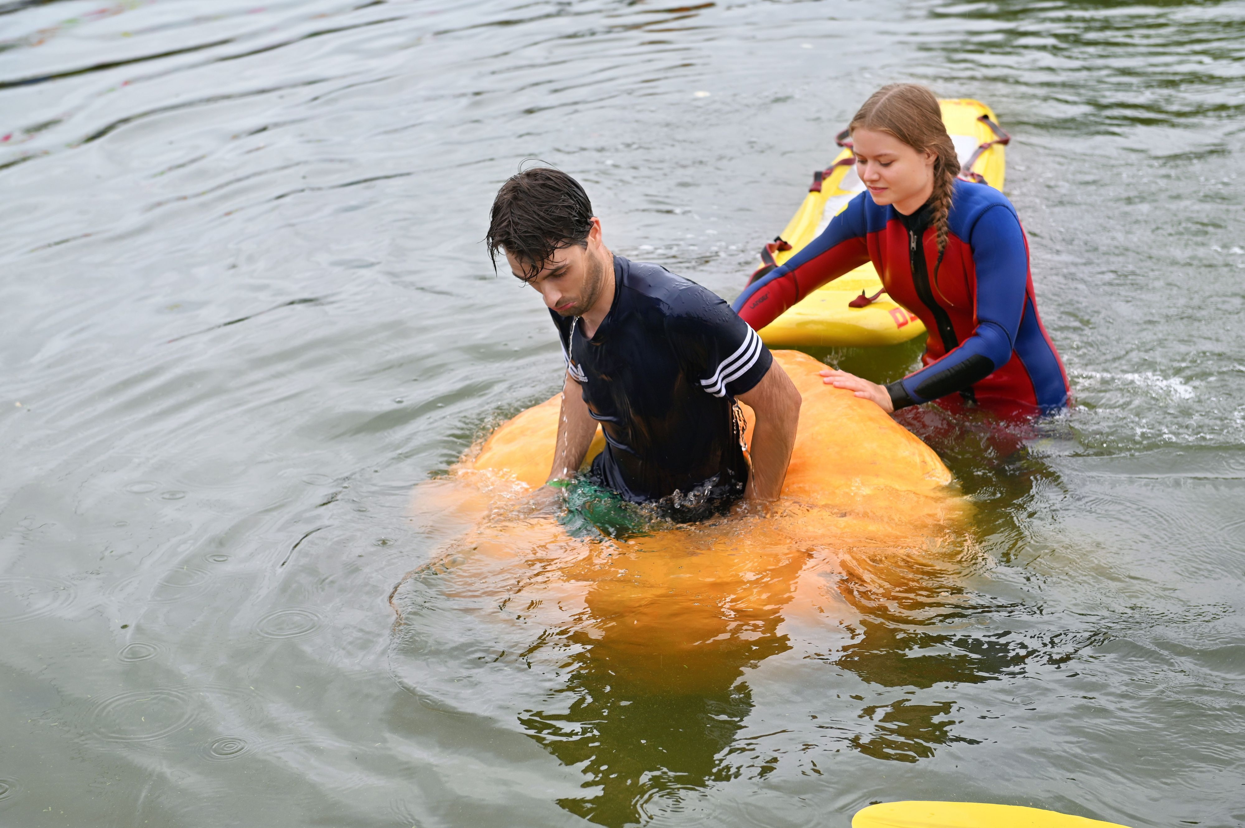 Ein Regatta-Teeilnehmer ist mit seinem Kürbisboot untergegangen; eine Helferin im Neoprenanzug ist bei ihm.