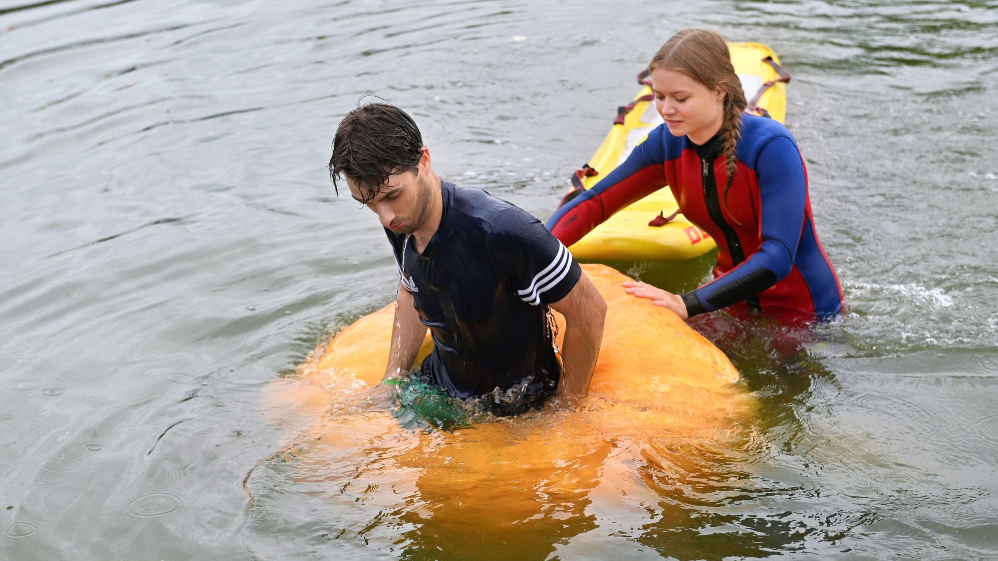 Ein Regatta-Teeilnehmer ist mit seinem Kürbisboot untergegangen; eine Helferin im Neoprenanzug ist bei ihm.