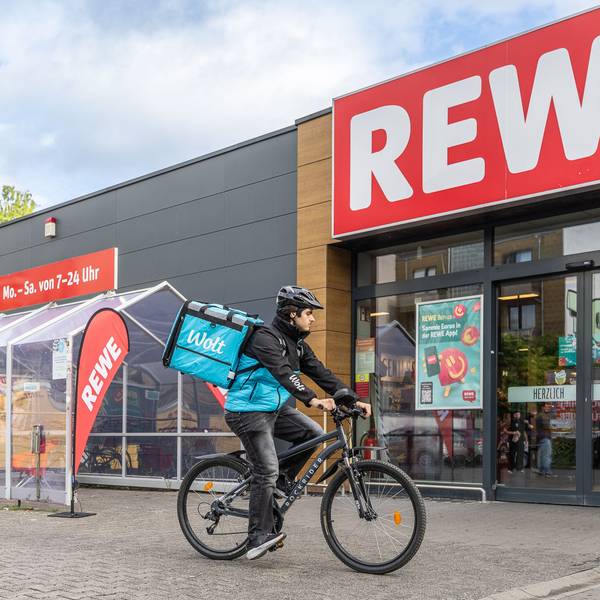 Ein Wolt-Fahrer hält auf seinem Rad vor einer Rewe-Filiale.