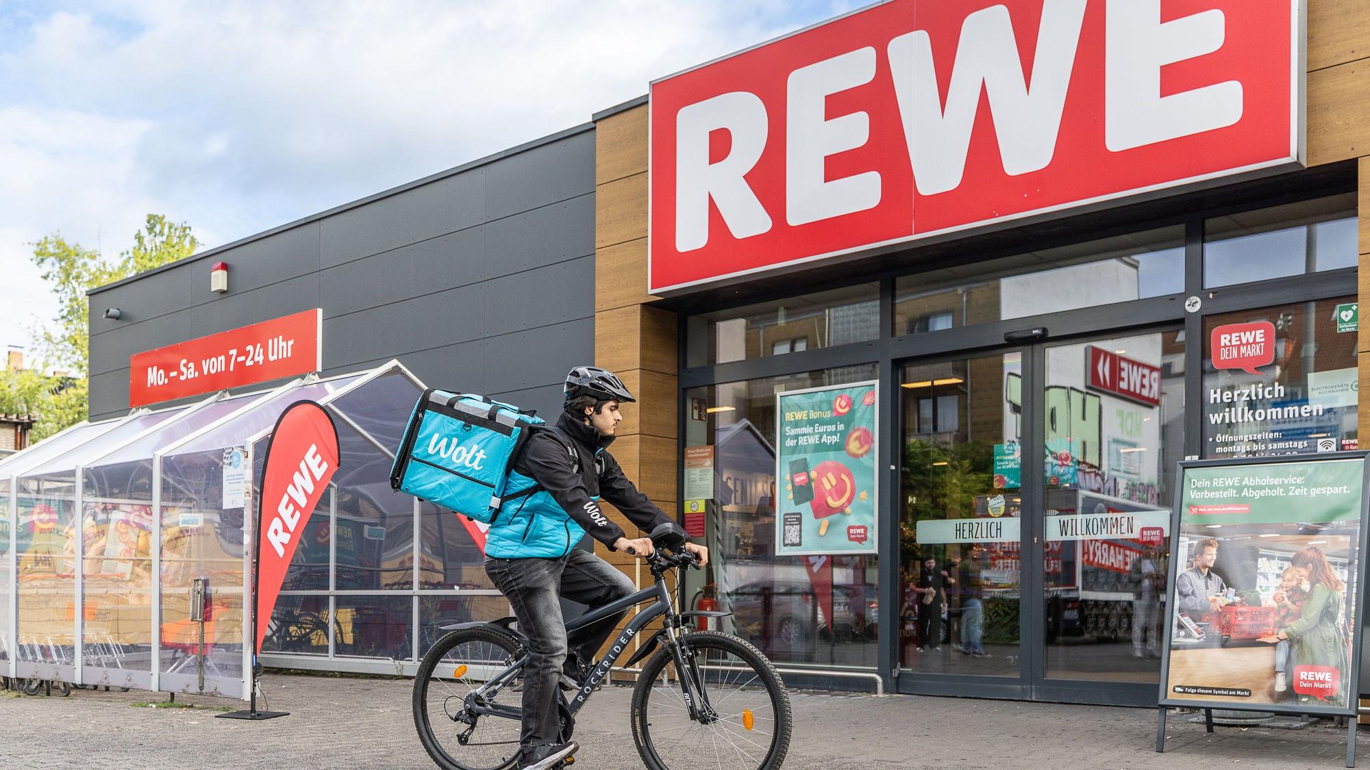 Ein Wolt-Fahrer hält auf seinem Rad vor einer Rewe-Filiale.