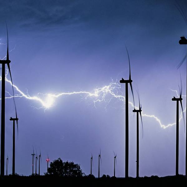 Das Symbolfoto zeigt einen mächtigen verzweigten Gewitterblitz, der die nächtliche Landschaft eines Windparks erleuchtet.
