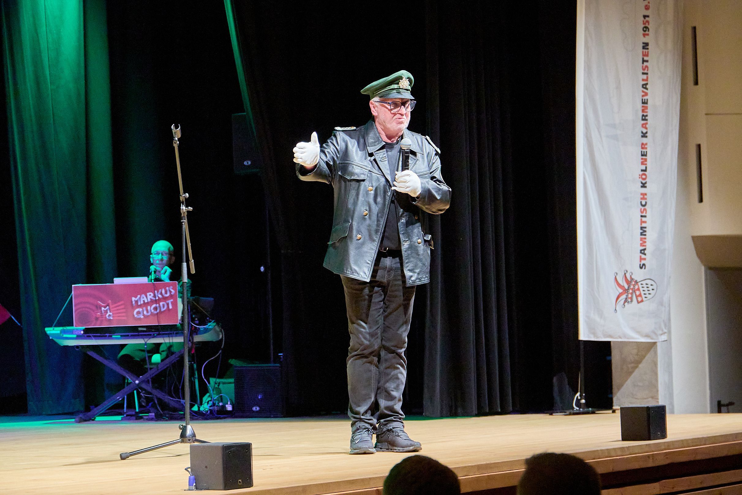 Ein mit einer altertümlichen Polizeiuniform verkleideter Mann steht auf der Bühne im Kursaal in Gemünd und spricht in ein Mikrofon.
