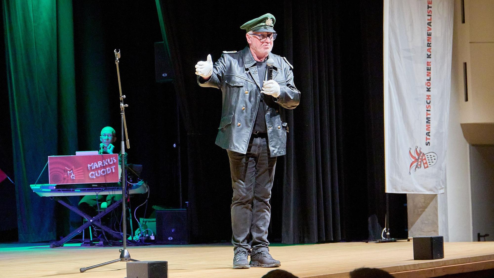 Ein mit einer altertümlichen Polizeiuniform verkleideter Mann steht auf der Bühne im Kursaal in Gemünd und spricht in ein Mikrofon.
