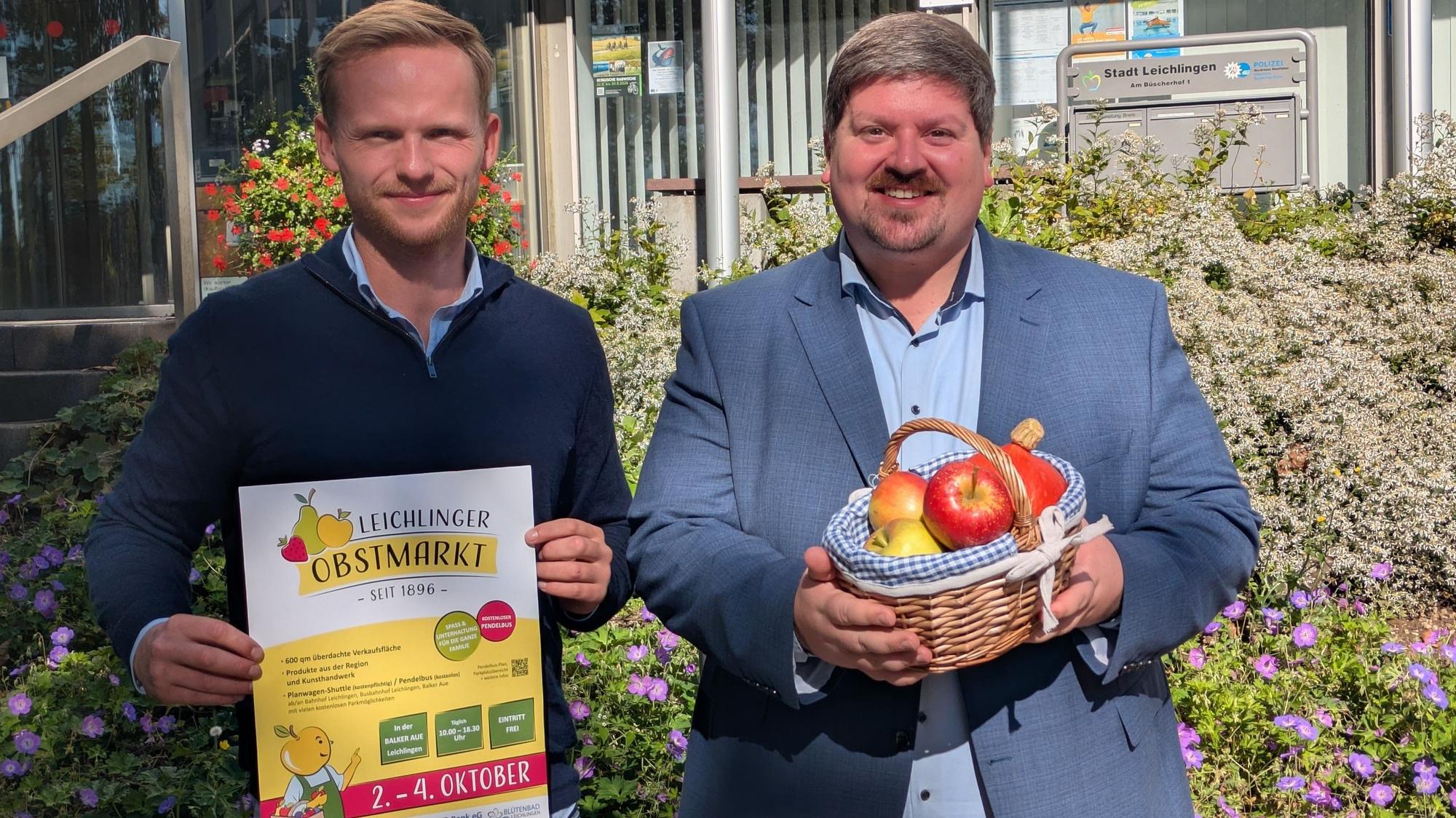 Zwei Männer halten ein Plakat und einen Obstkorb.