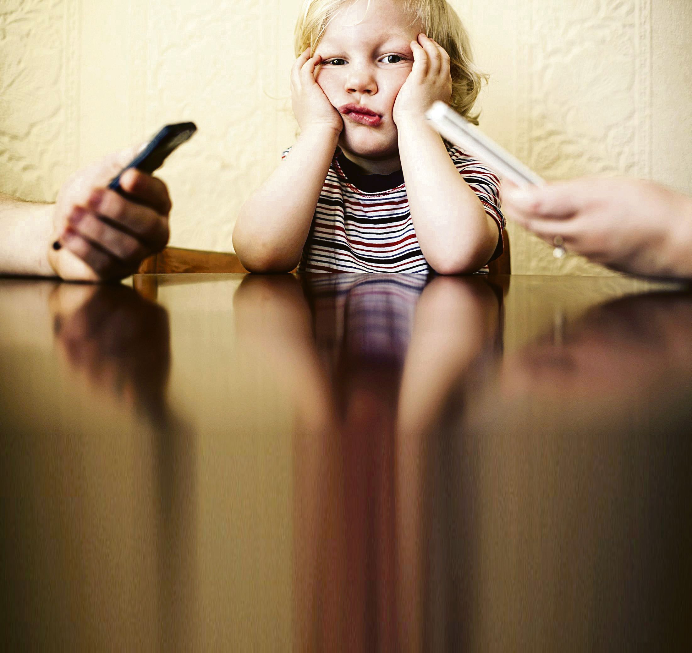Little boy sitting and looking bored while his parents are busy using their smart phones. *** Local Caption *** 2.142322603