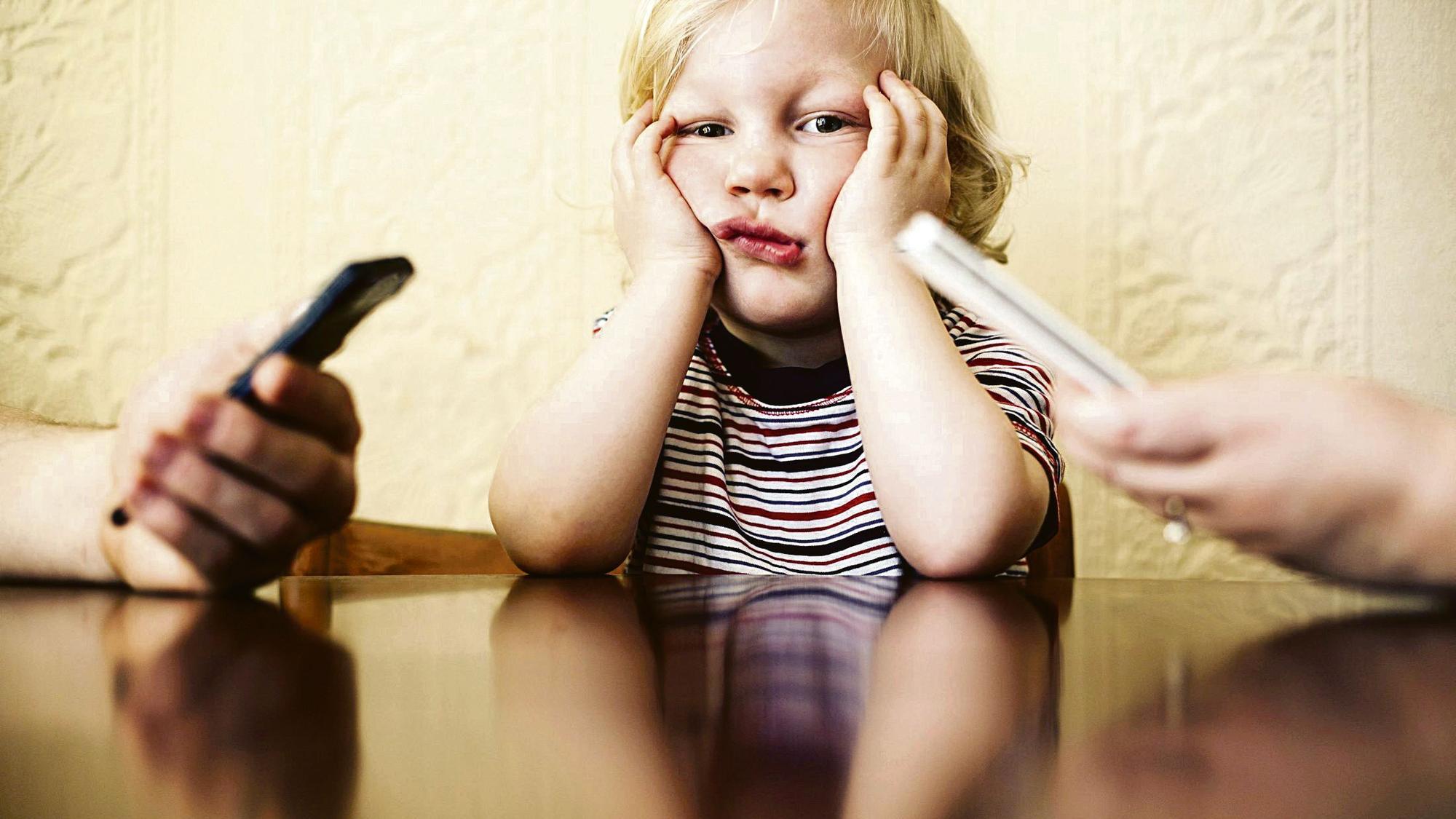 Little boy sitting and looking bored while his parents are busy using their smart phones. *** Local Caption *** 2.142322603