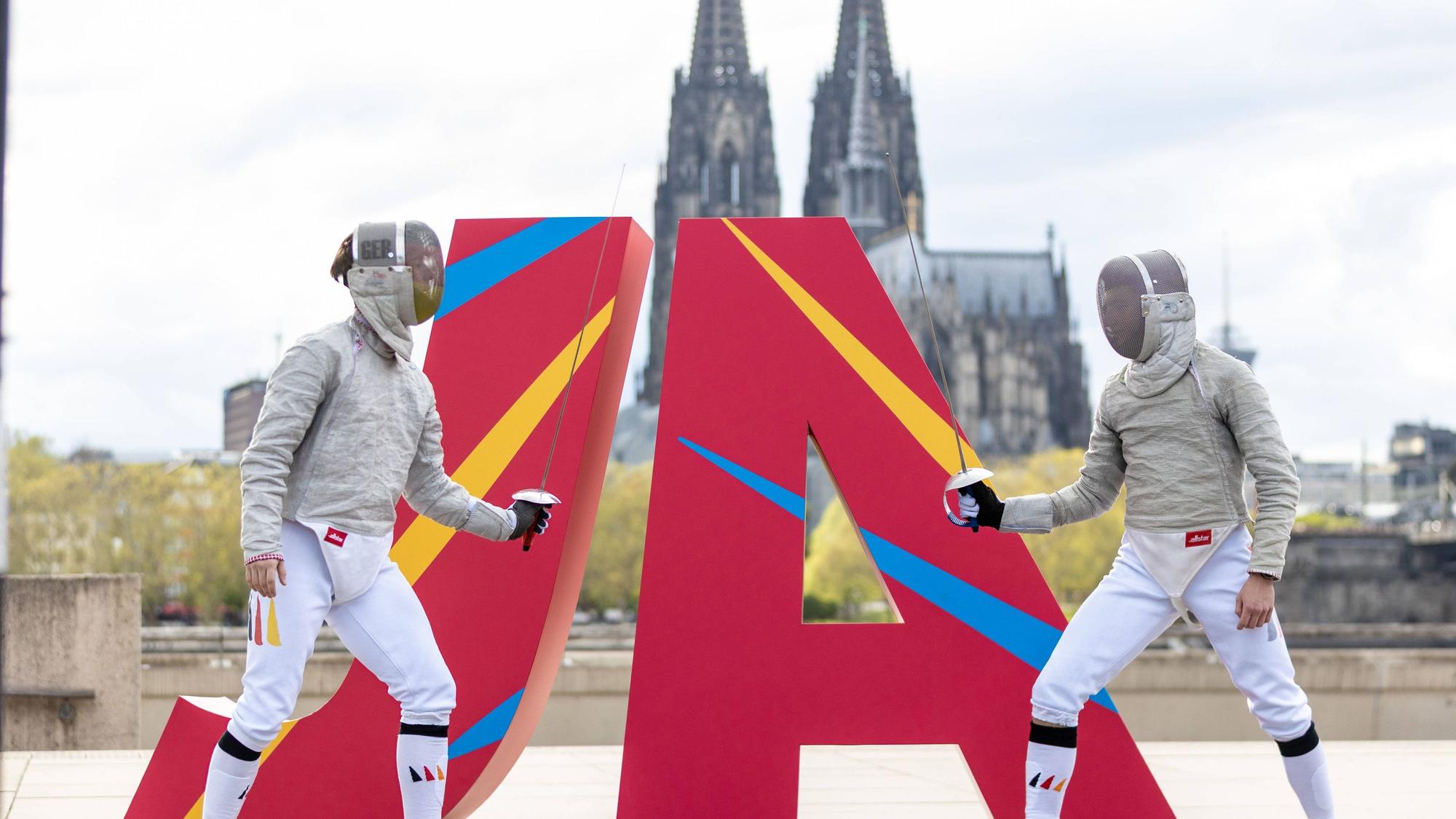 Zwei Fechter vor eine JA Logo vor dem Kölner Dom.