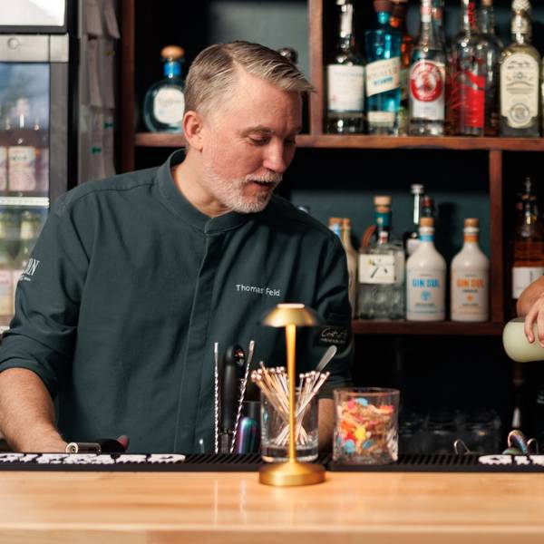 Zwei Männer in dunkler Bartender-Kleidung stehen hinter einer Theke.