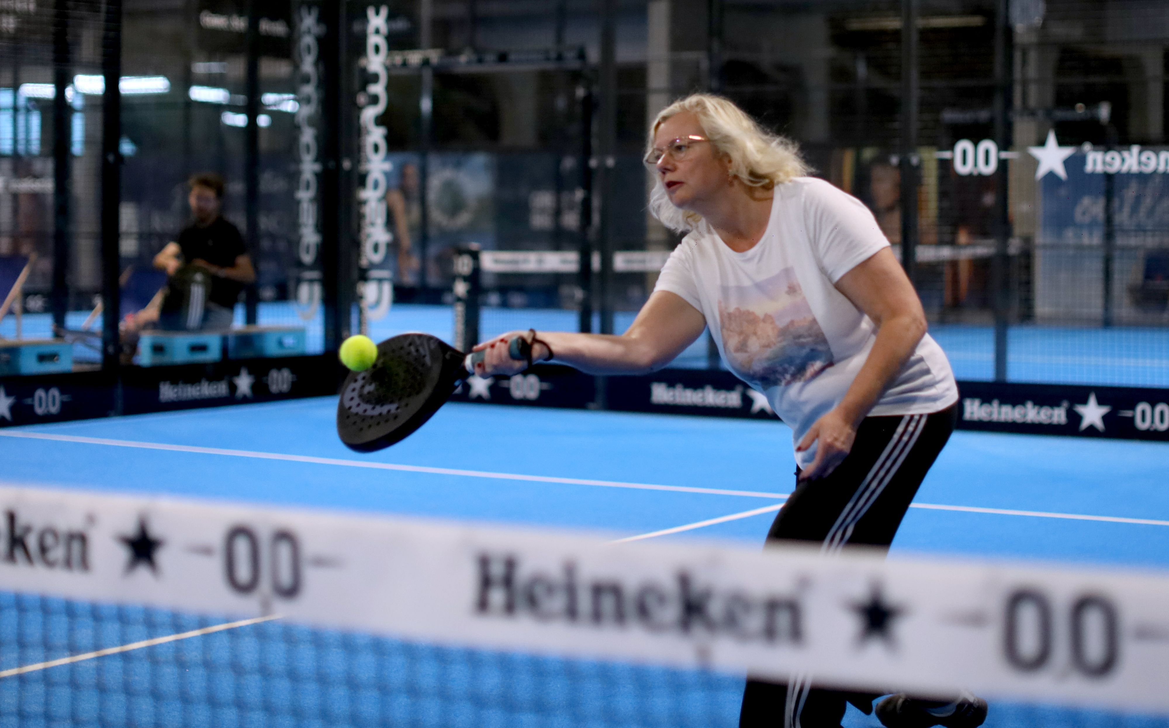 Eine blonde Frau steht auf einem Padel-Court und spielt den Ball.