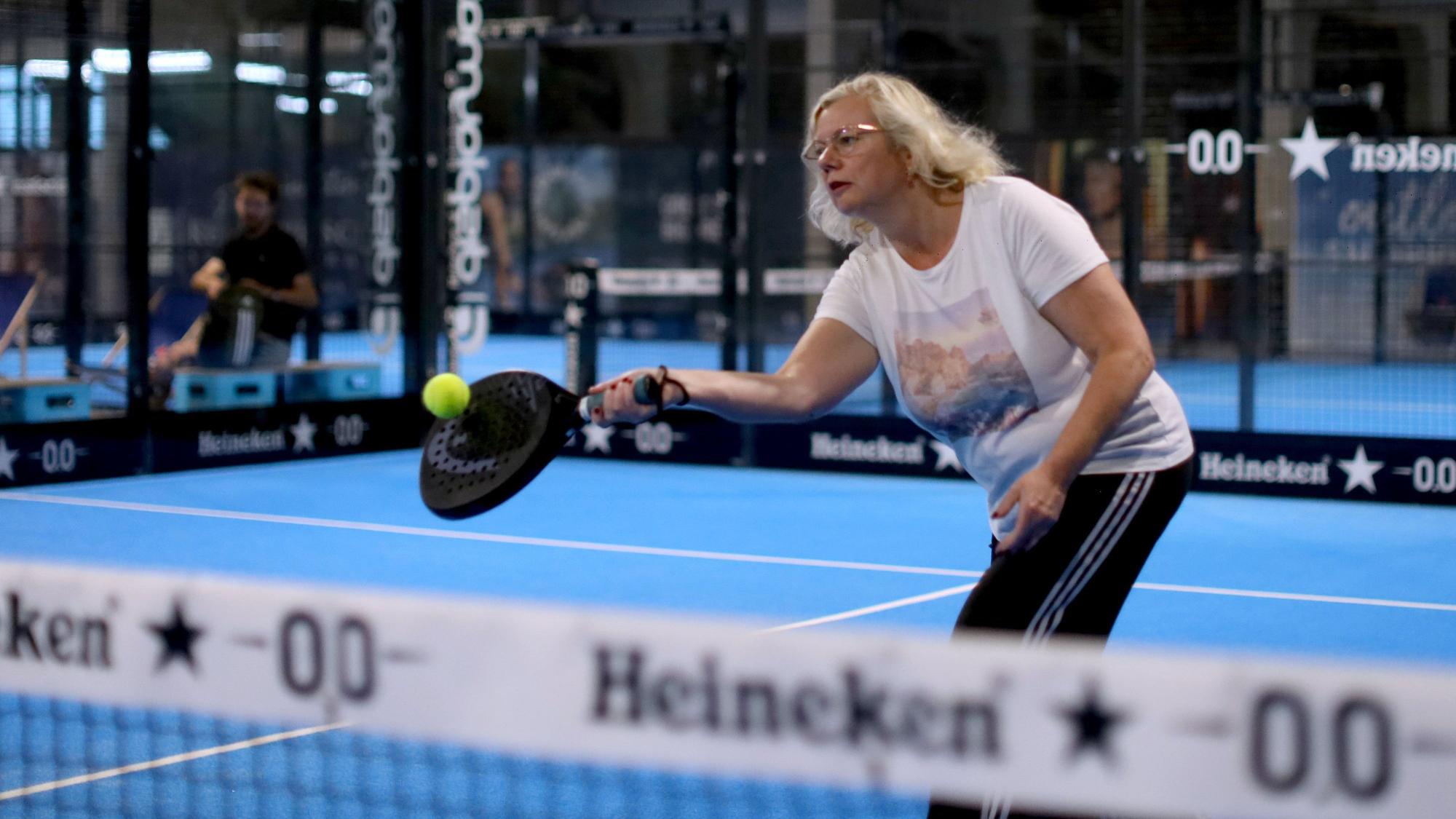 Eine blonde Frau steht auf einem Padel-Court und spielt den Ball.