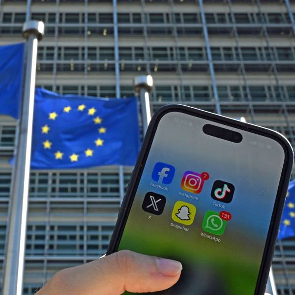 Eine Person hält ein Smartphone mit den Logos der Social-Media-Apps Facebook, Instagram, TikTok, X, Snapchat und WhatsApp vor Fahnen der Europäischen Union und dem Gebäude der Europäischen Kommission. Die EU-Kommission will den Zugang zu Social Media für Kinder einschränken.