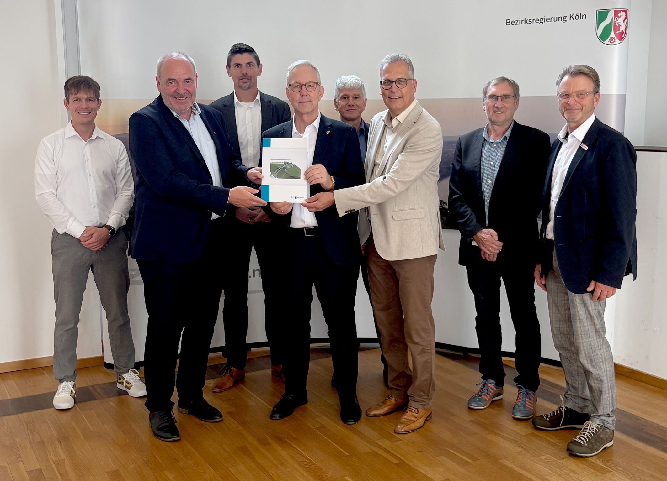Eine Gruppe Männer hat sich versammlet, drei halten eine Mappe mit den Antragsunterlagen.
