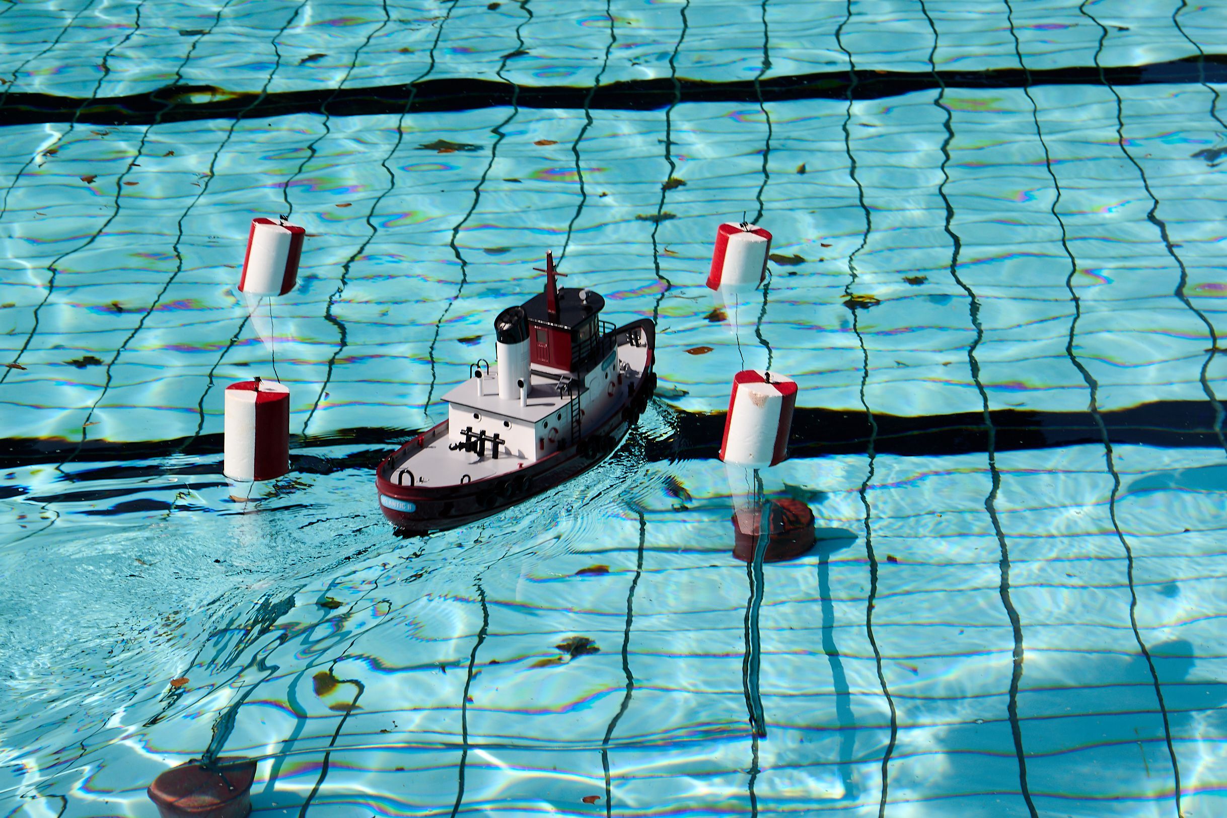 Ein Modellboot steuert zwischen vier rot-weißen Schwimmbojen hindurch.