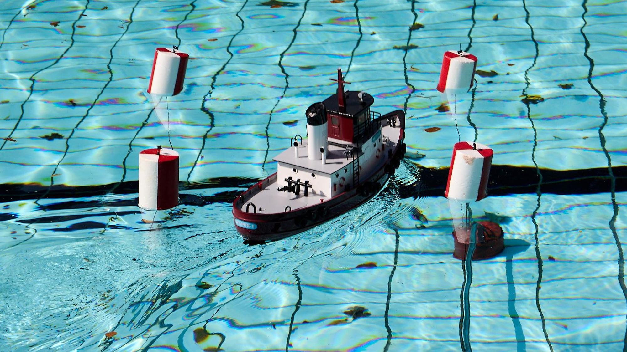 Ein Modellboot steuert zwischen vier rot-weißen Schwimmbojen hindurch.