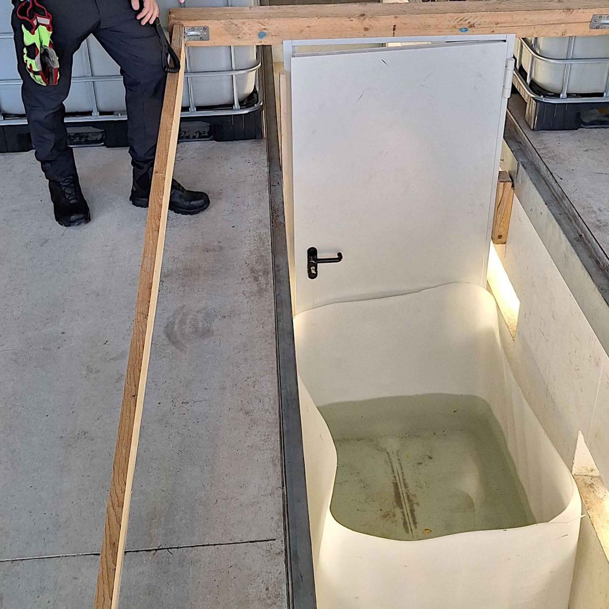 Das Bild eine Tür, vor der eine Wanne mit Wasser steht.