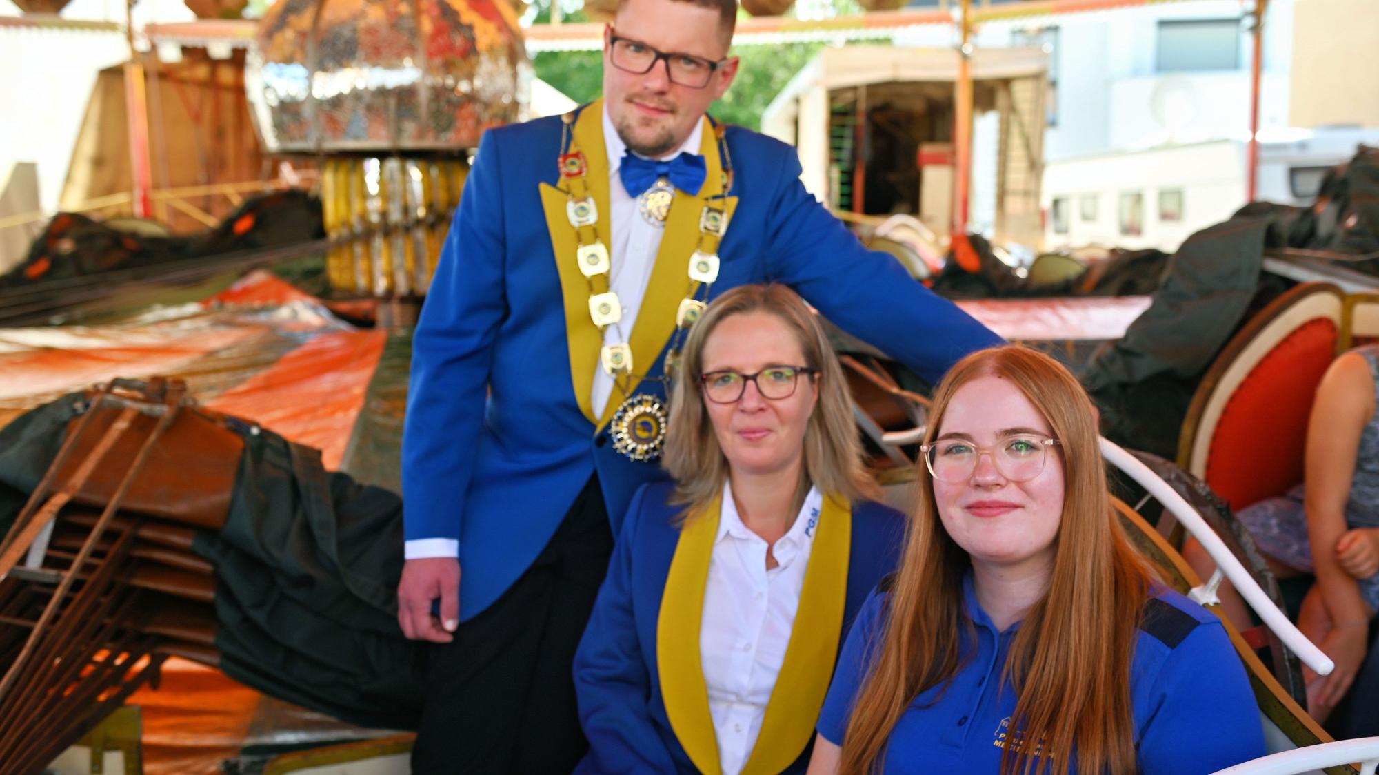Die drei Genannten tragen das blaue Outfit ihres Karnevalsvereins und posieren vor einem Kirmeskarussell für den Fotografen.
