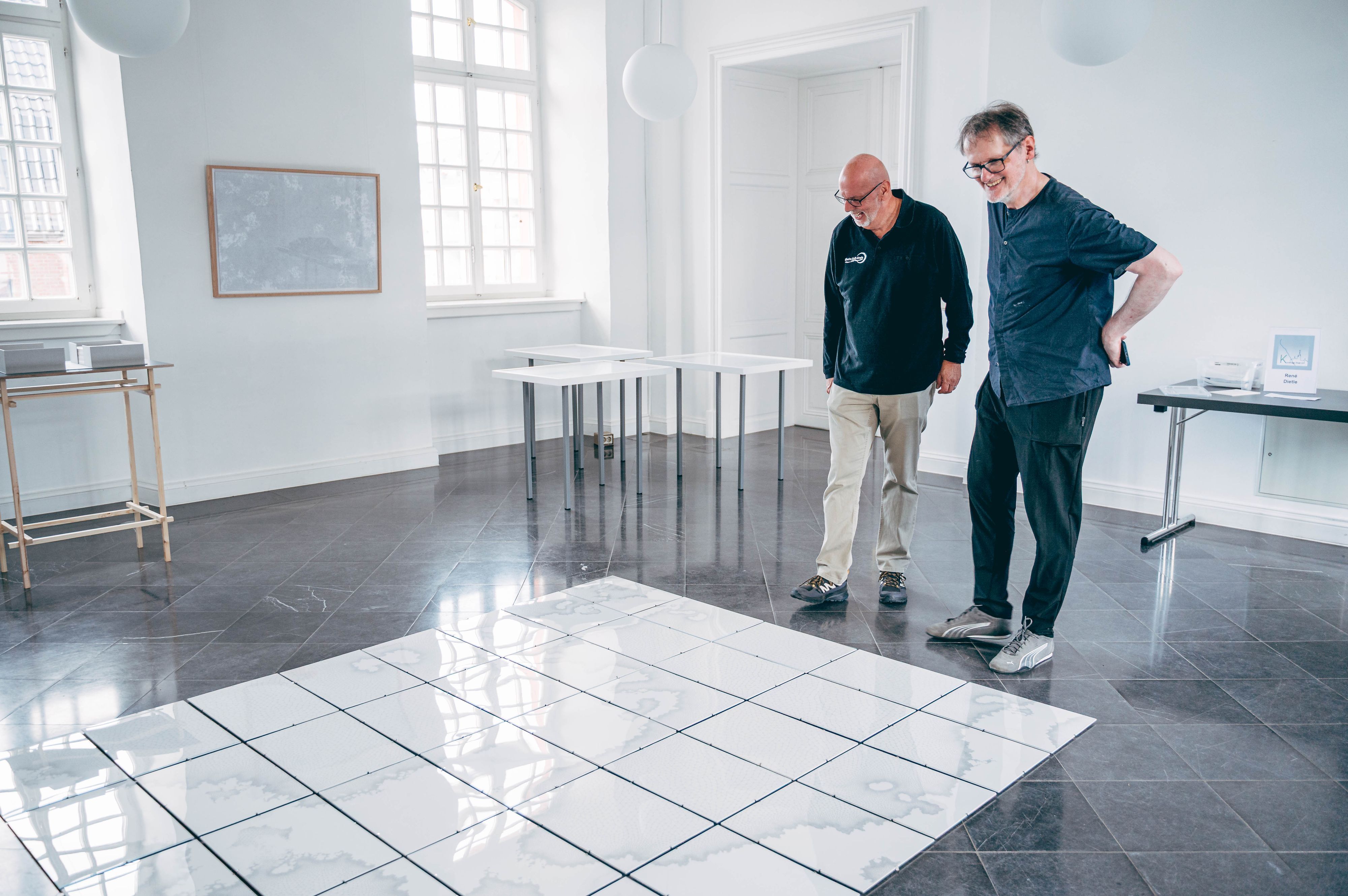 Auf dem Bild sind zwei Männer vor einem Bodenkunstwerk zu sehen.