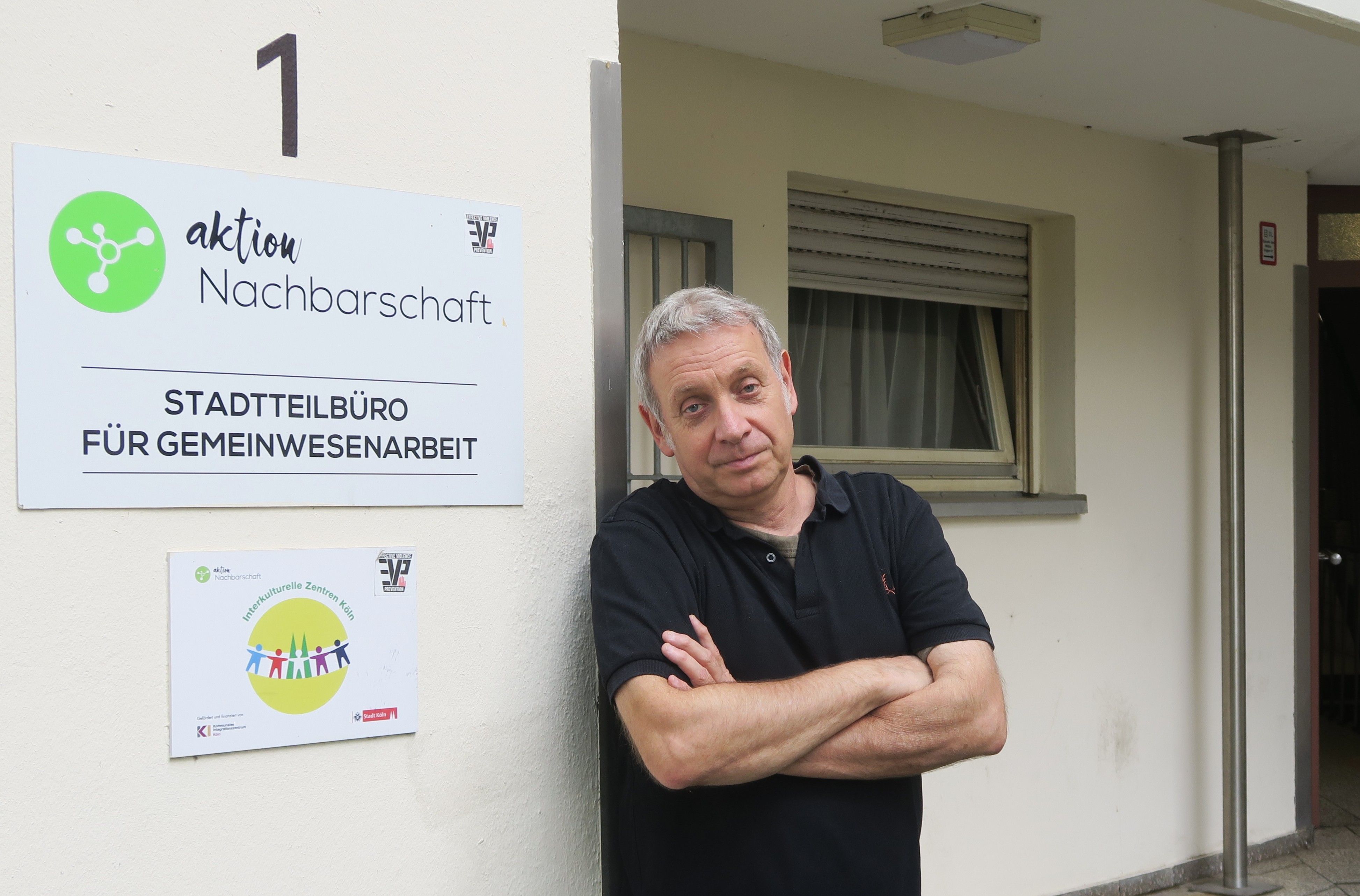Ein Mann im schwarzen Poloshirt lehnt an einer Hauswand.