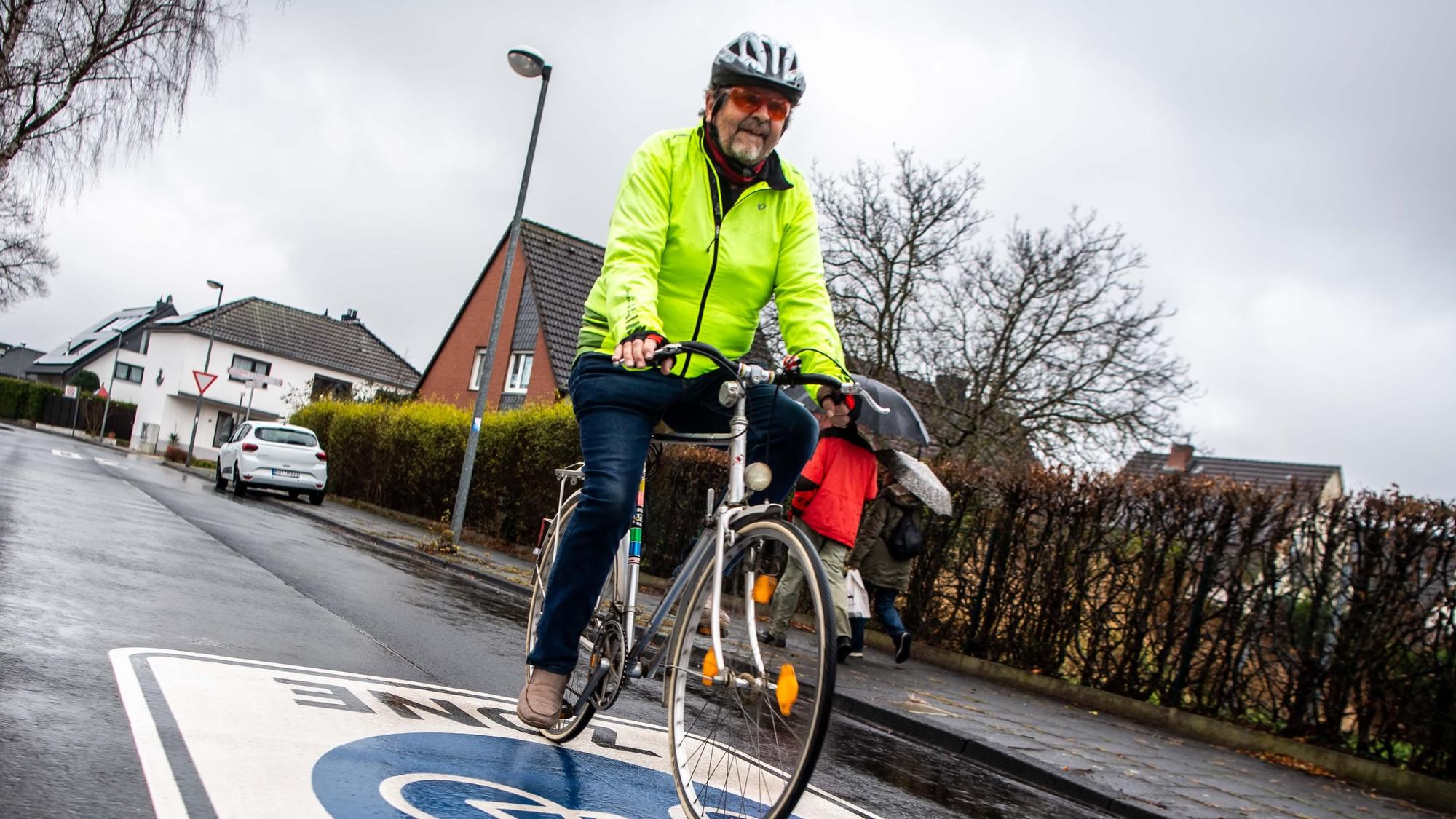 Das Bild zeigt einen Radfahrer mit Helm und leuchtend gelber Jacke in einem Wohngebiet.