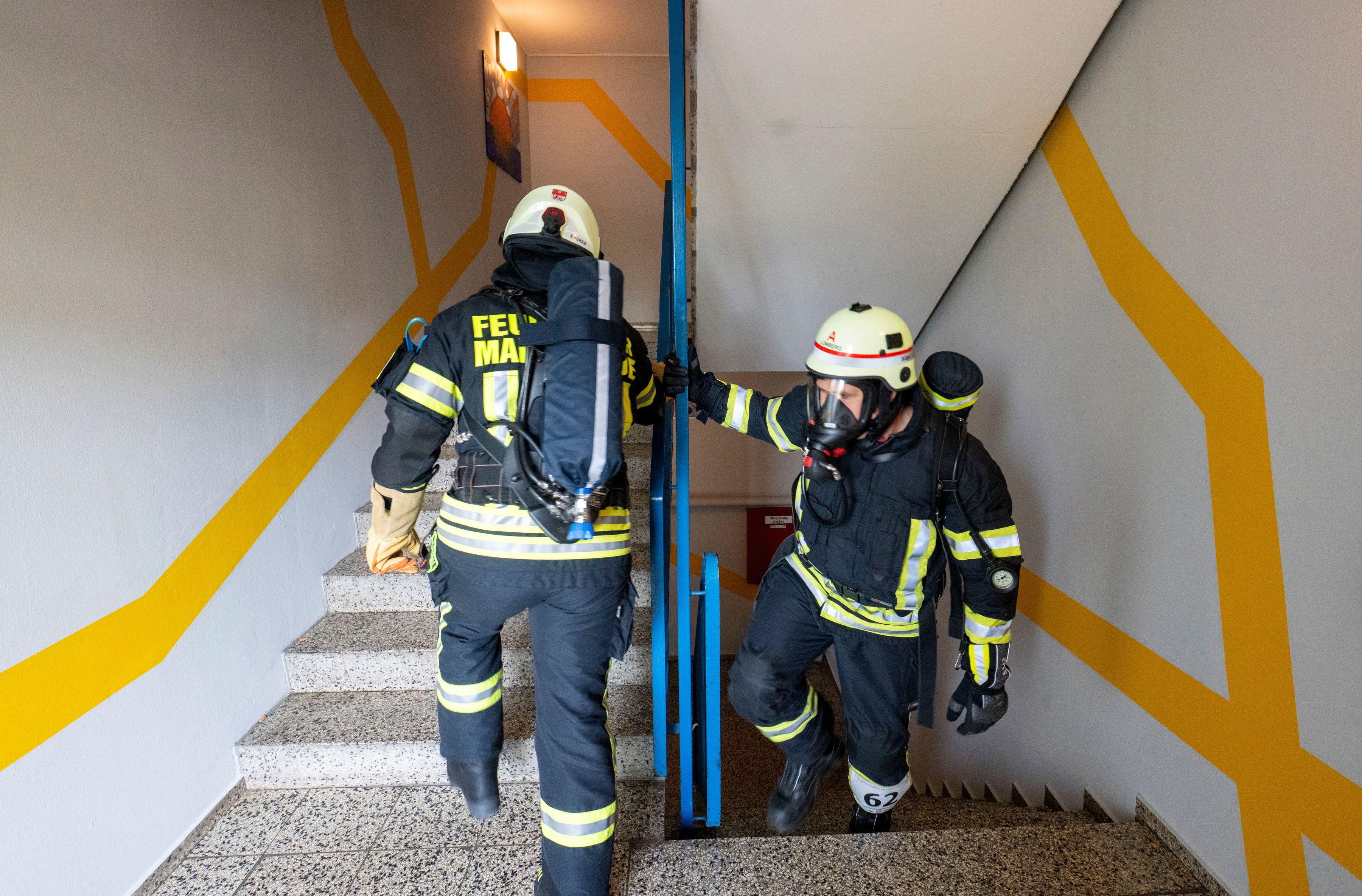 Feuerwehrleute ersteigen die Treppen in voller Montur mit Atemschutzgeräten.