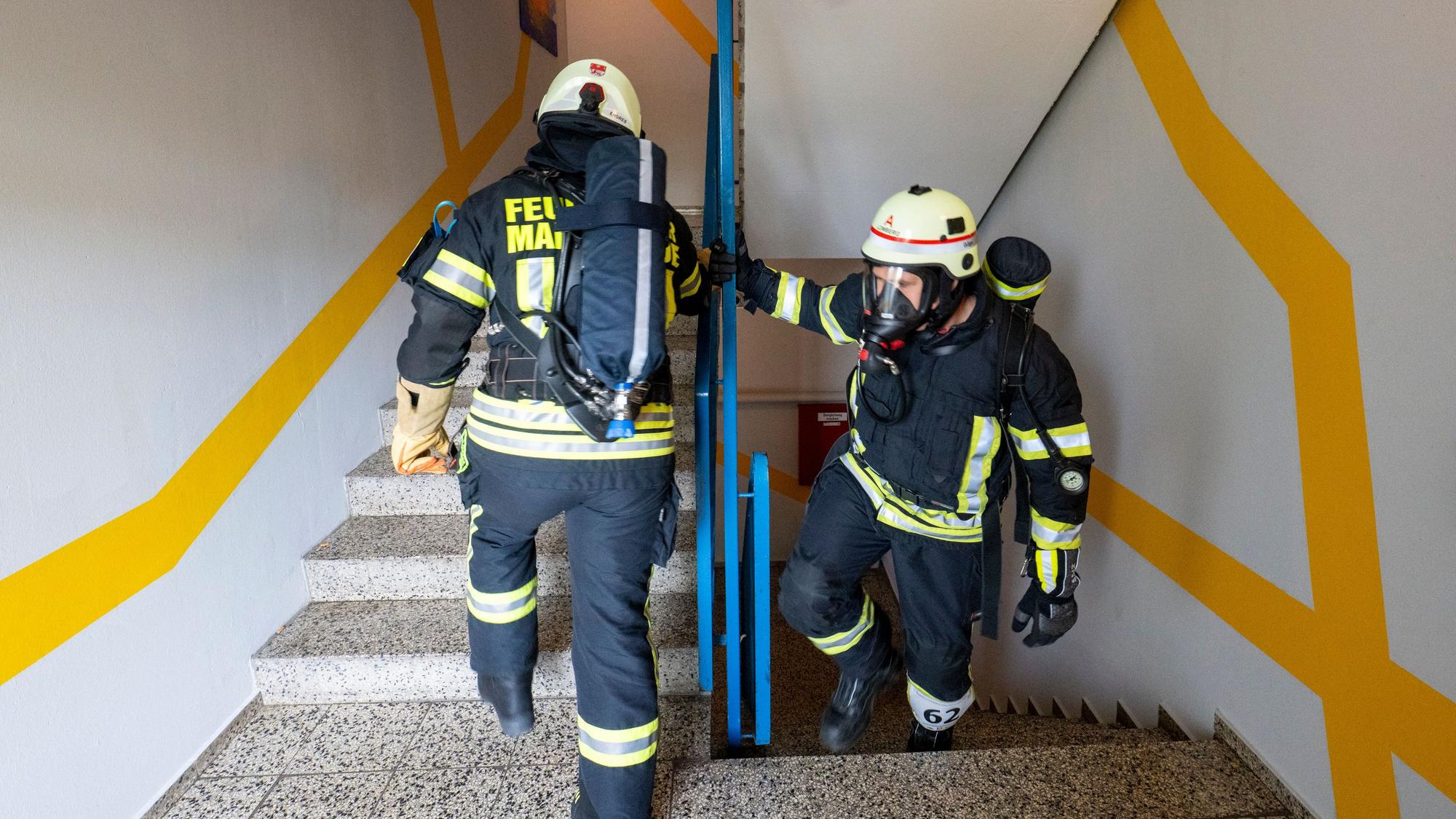 Feuerwehrleute ersteigen die Treppen in voller Montur mit Atemschutzgeräten.
