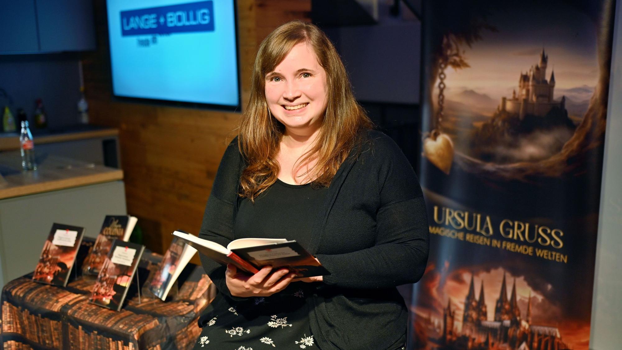 Autorin Ursula Gruß mit einem aufgeschlagenen Buch in der Hand vor einem Roll-up mit ihrem Namen.